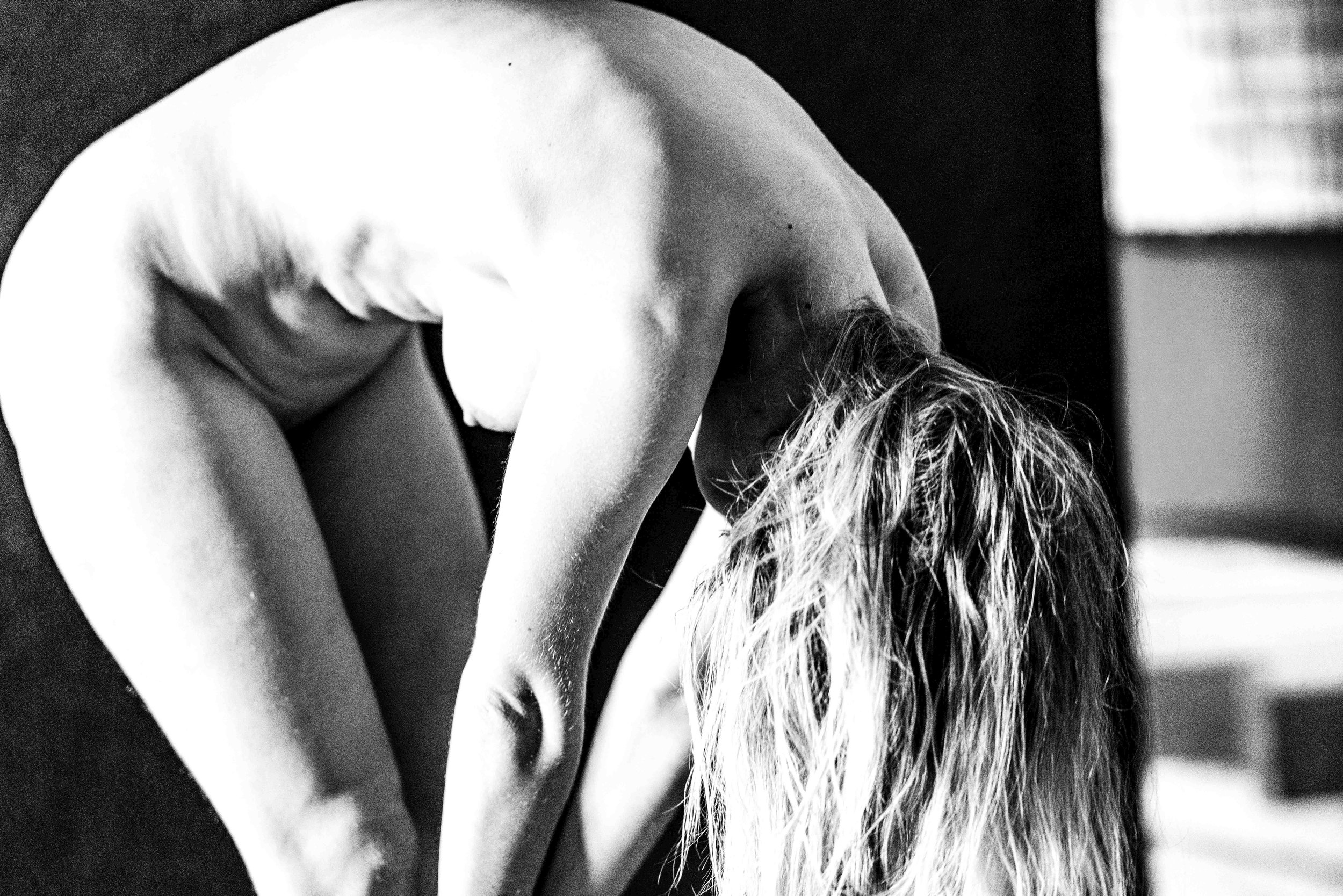 Black and white photo of a woman bent forward, with her long hair hanging down. Her face is not visible.