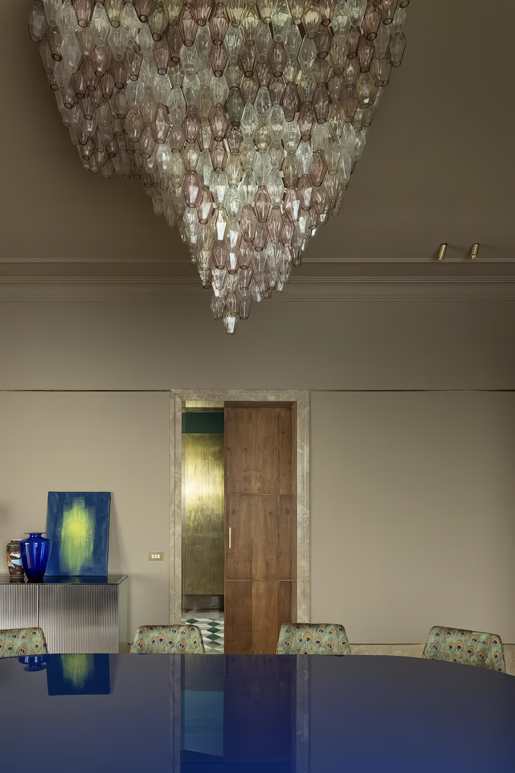 Close-up of pink and clear glass chandelier above a blue dining table.