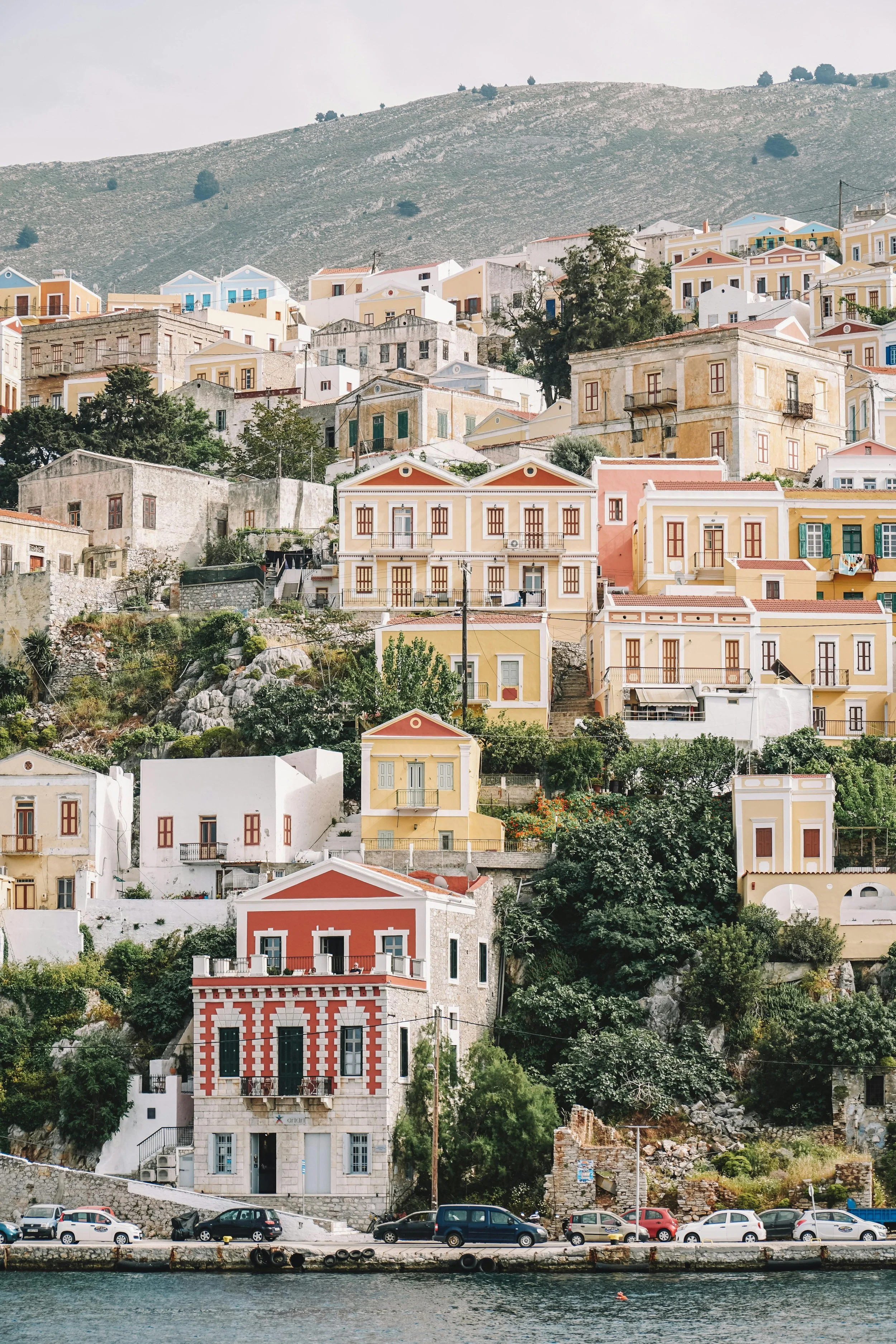 Colorful buildings on a hillside by a body of water, with cars parked along the shore.