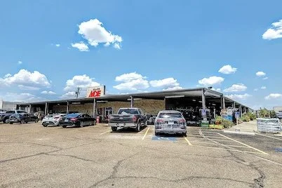 A parking lot in front of an Ace Hardware store under a blue sky with white clouds