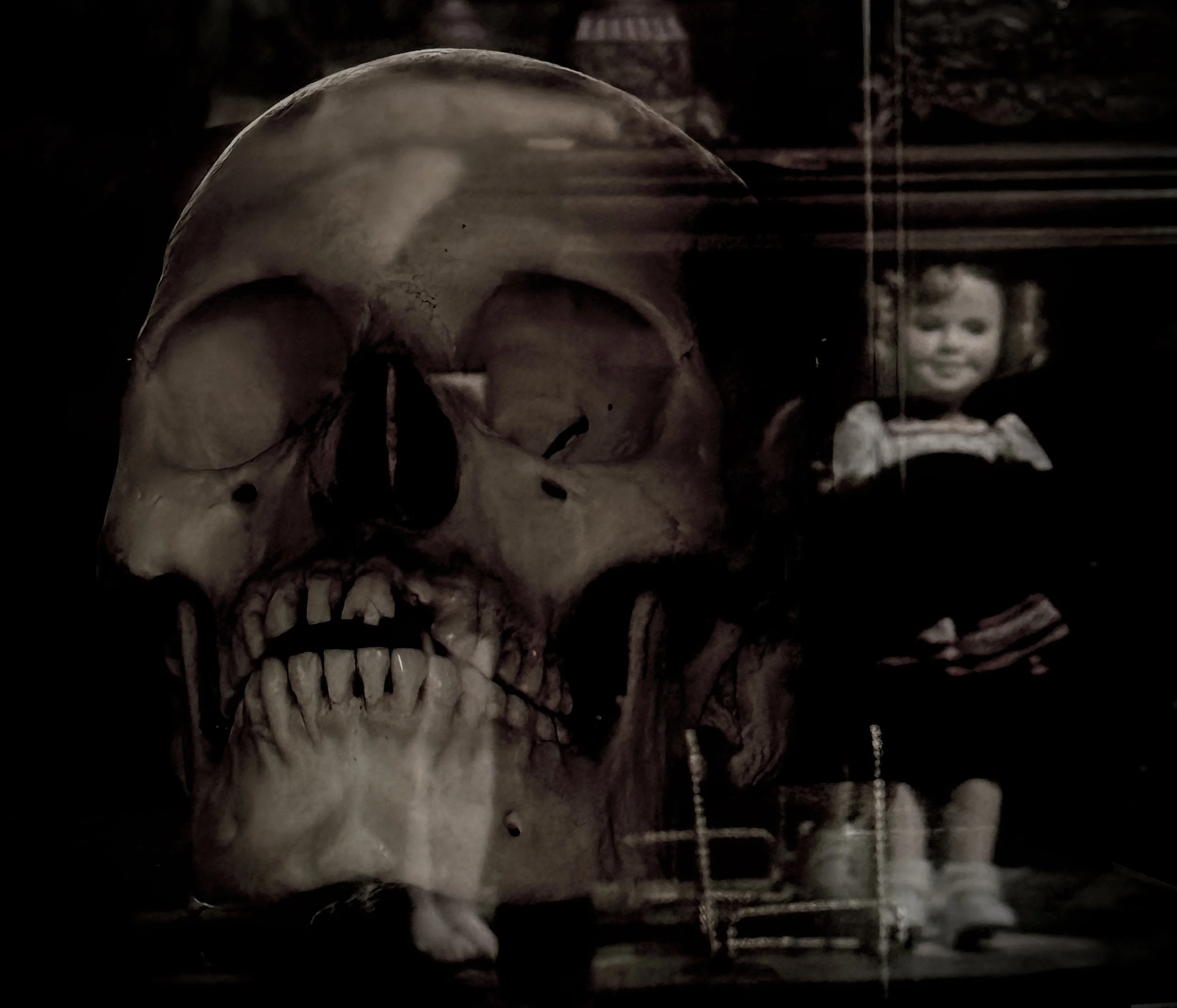 A human skull with a child doll beside it, behind a reflective glass surface with tape on the sides.
