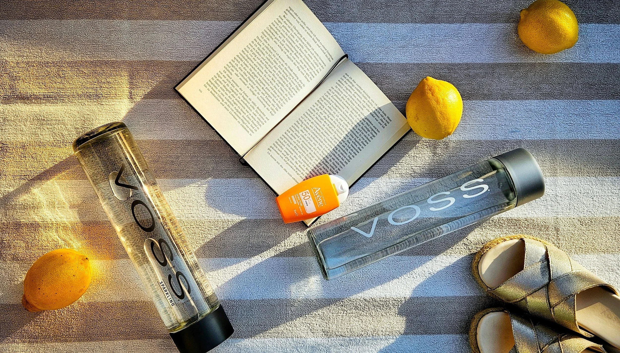beach day essentials including water bottle sunscreen book and sandals on striped towel