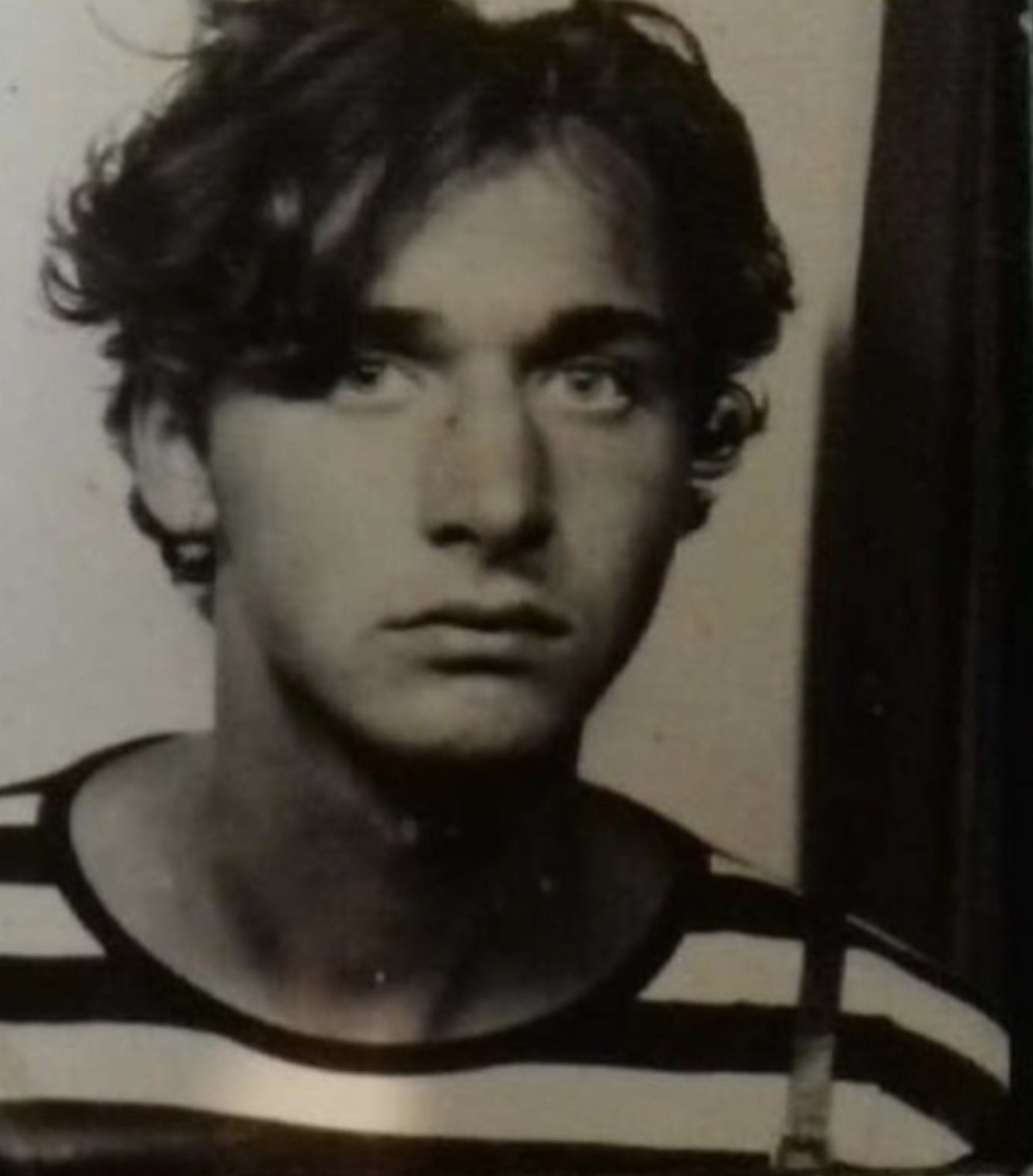 Black and white portrait of a person with short curly hair, wearing a striped shirt, looking directly at the camera with a serious expression.