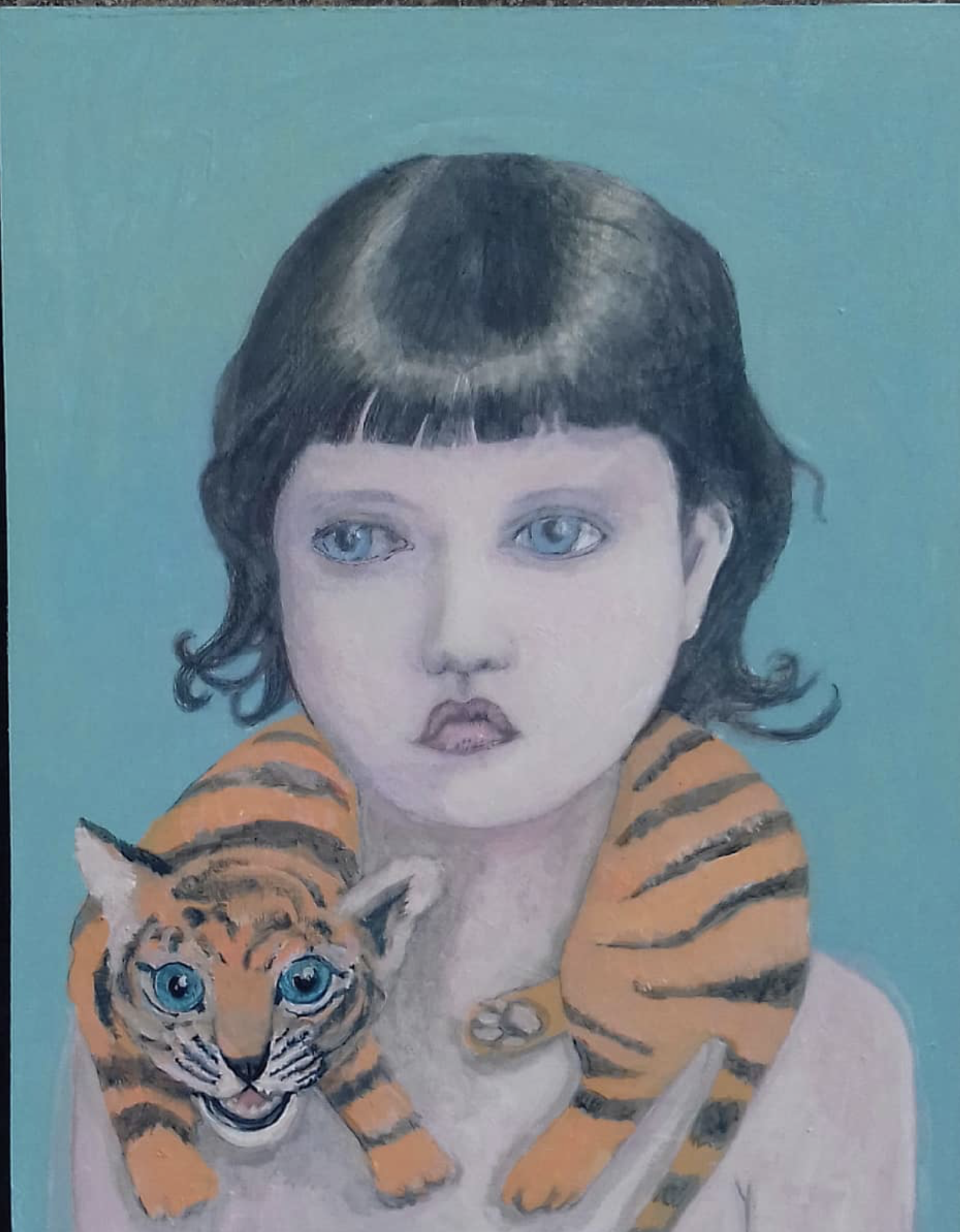 A portrait of a young girl with light skin, blue eyes, short dark hair with bangs, wearing a tiger-striped shirt, and a small tiger cub with blue eyes sitting on her shoulder against a teal background.