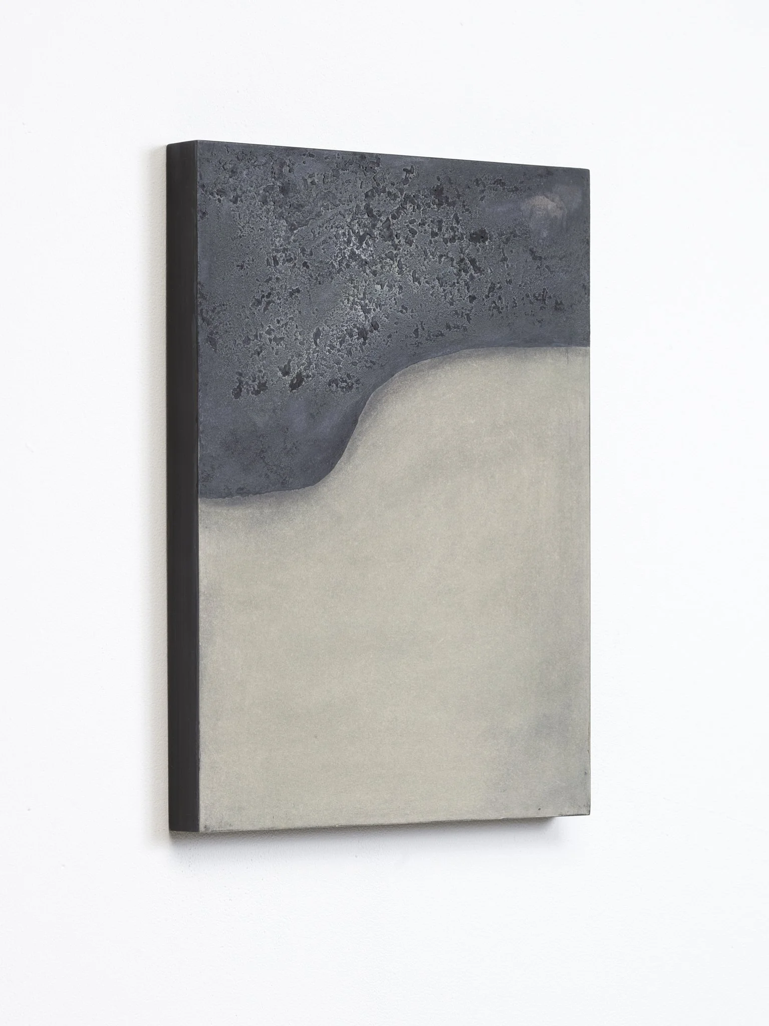 Close-up of a rectangular artwork with a textured black upper section and a smooth light lower section, mounted on a plain white wall.