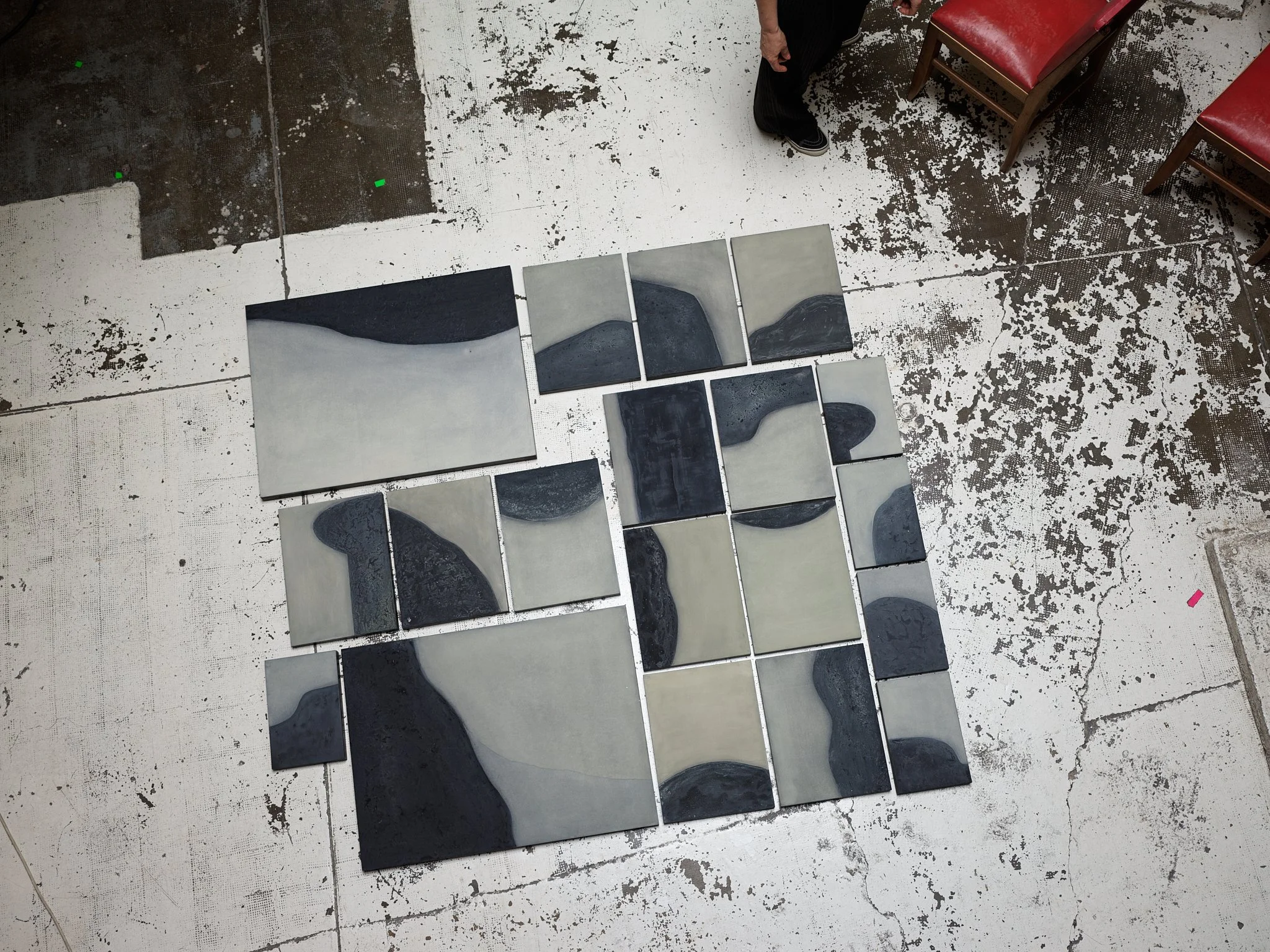 A person standing next to a display of nine abstract black and white landscape paintings on a tiled floor, with two red chairs nearby.