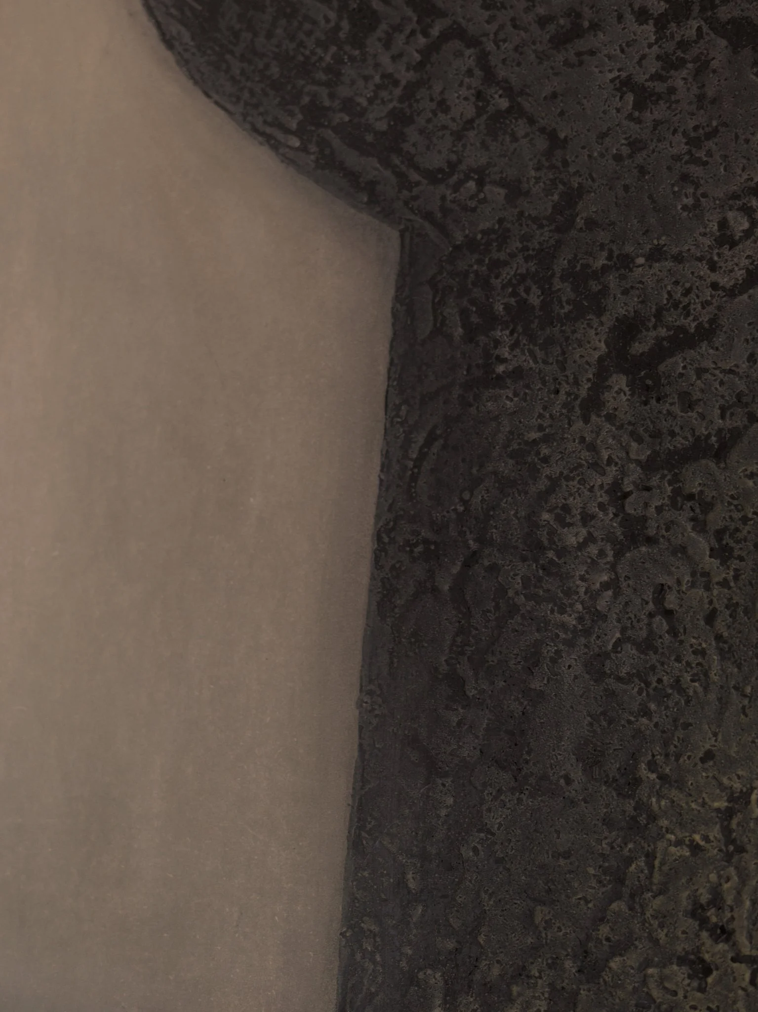 Close-up of a corner where a smooth, light-colored wall meets a textured dark surface, possibly a black granite counter or flooring.