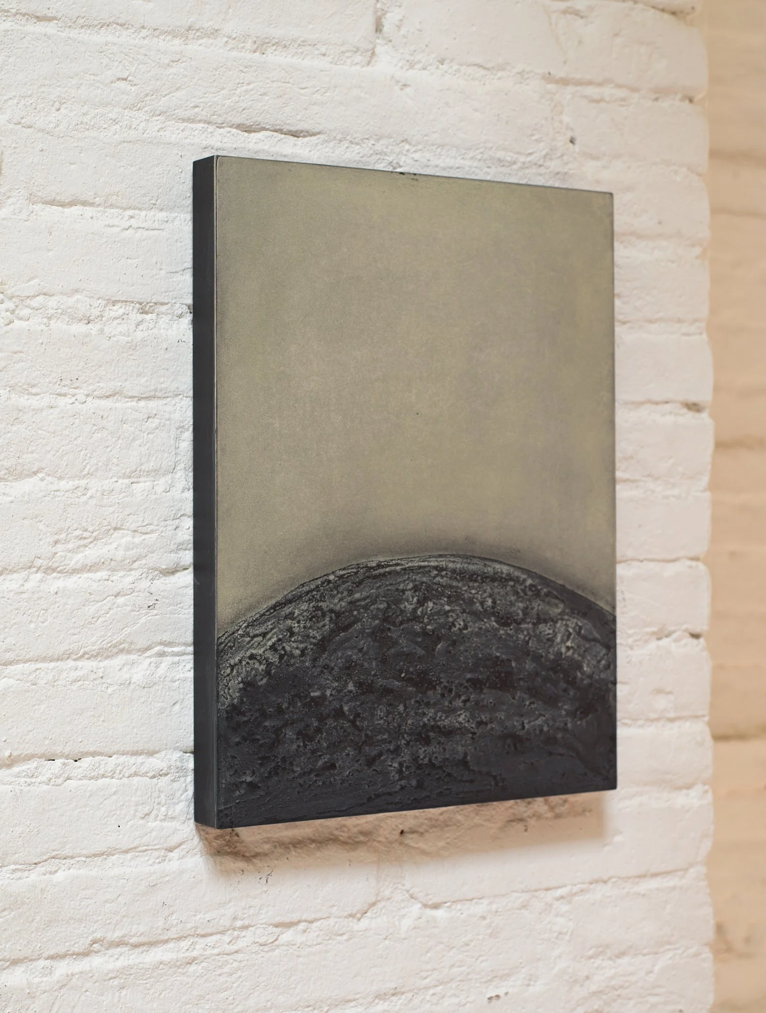 Abstract mixed-media artwork by Ekaterina Galera displayed on a white brick wall, showing a dark textured soft form.