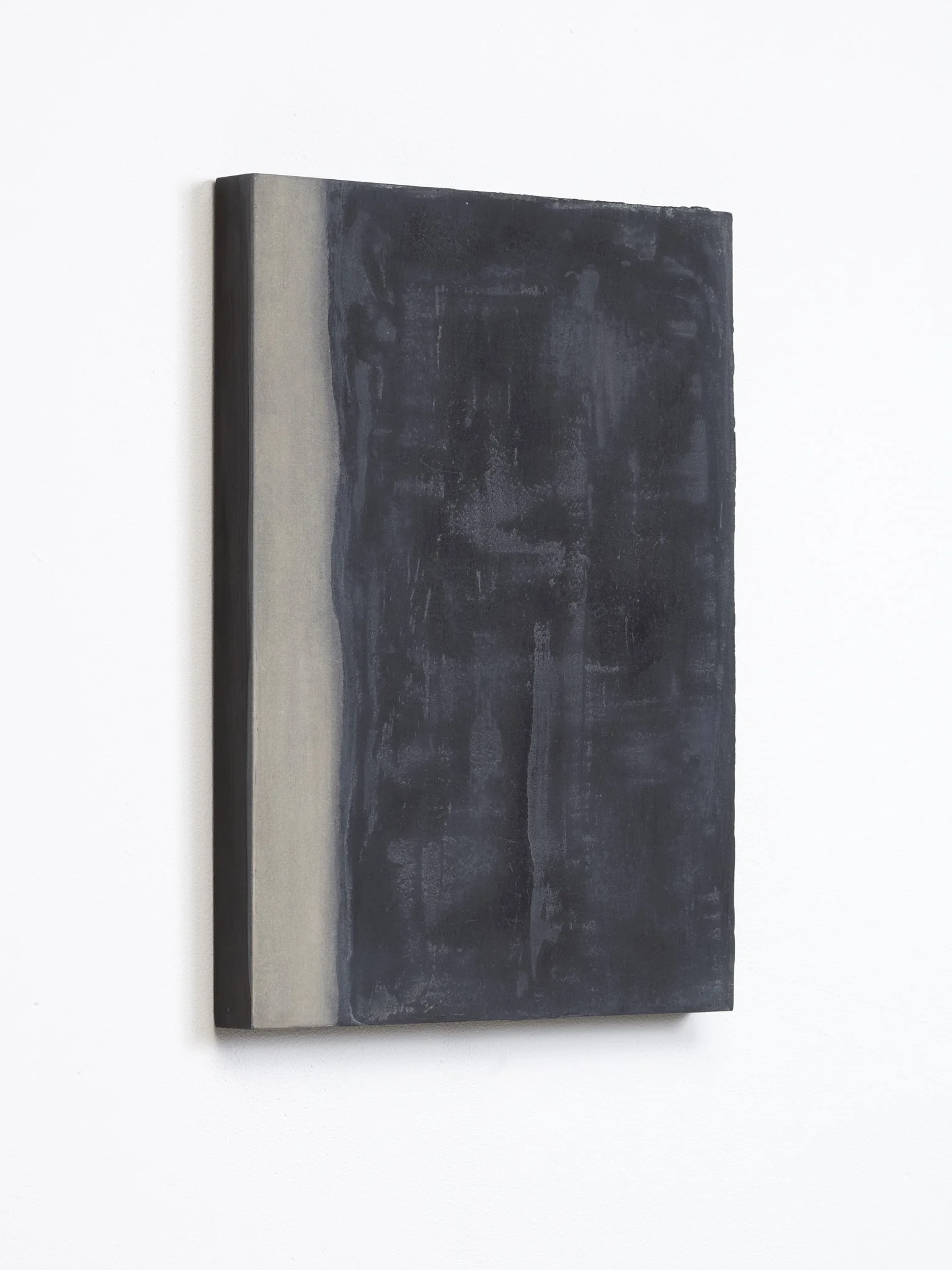 A rectangular, abstract dark gray and light gray painting with textured surface, mounted on a white wall.