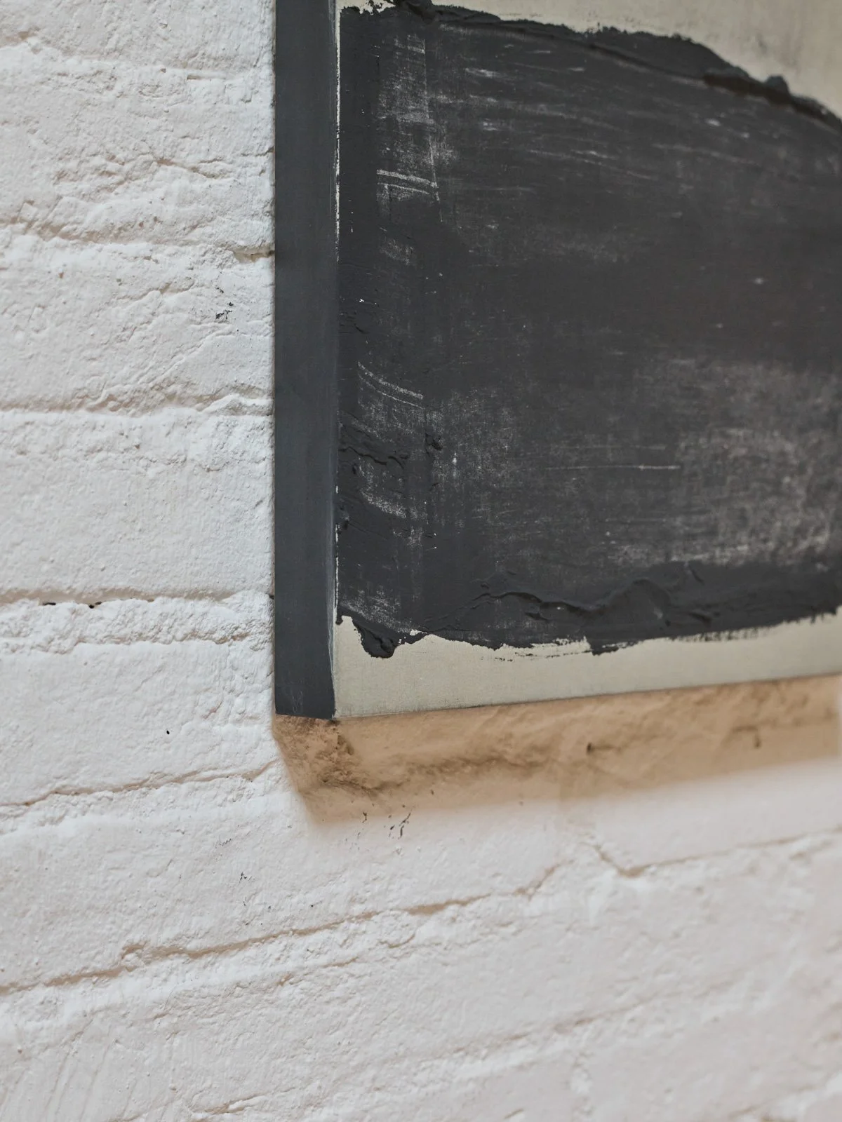 Abstract mixed-media artwork by Ekaterina Galera displayed on a white brick wall, showing a dark textured geometric form.