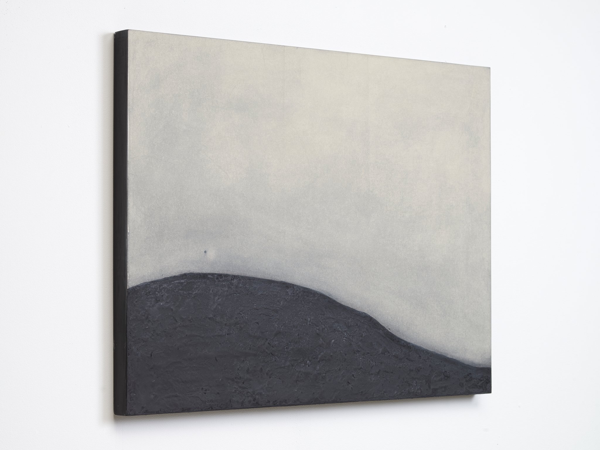 A rectangular artwork depicts a minimalistic scene with a flat, dark gray rock formation occupying the bottom third of the frame, and a smooth, light gray sky filling the top two-thirds. The composition is simple and abstract.