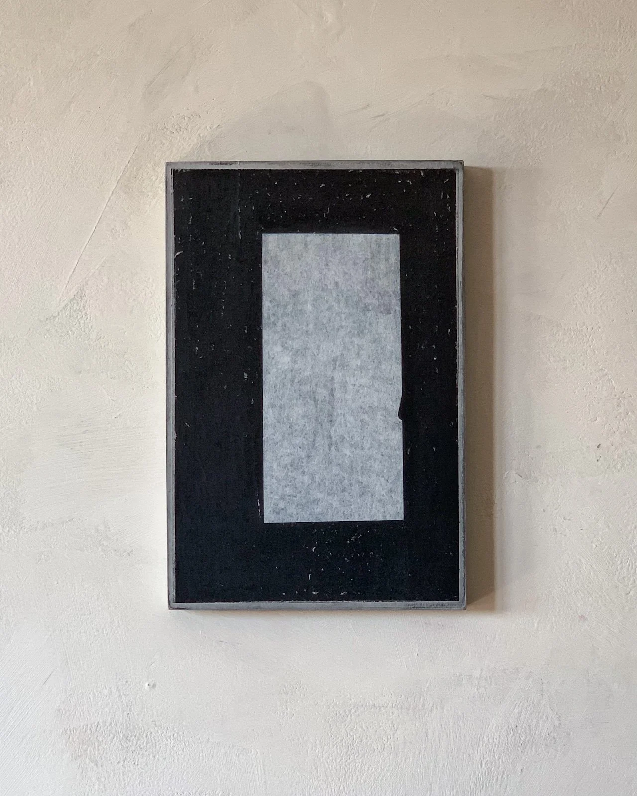 A black framed picture with a central gray rectangle on a beige wall.