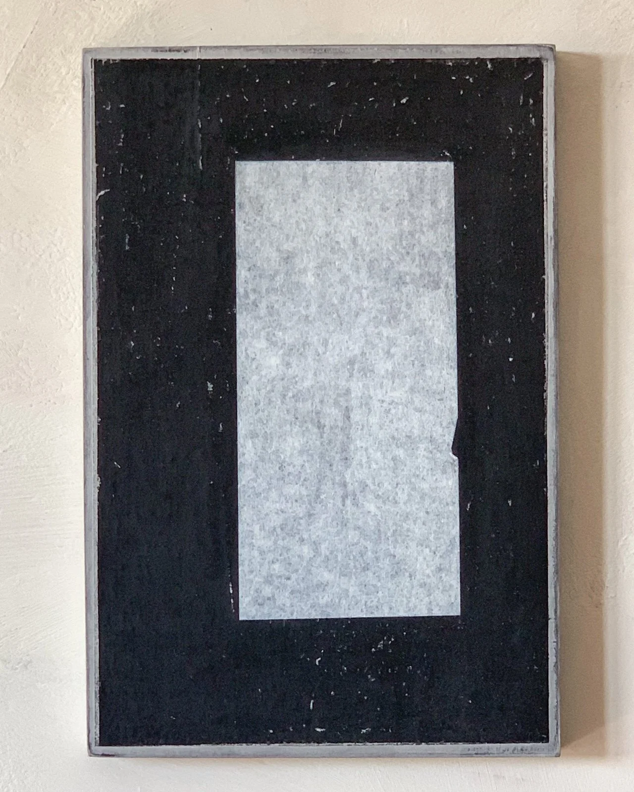 A black and gray framed chalkboard with a blank gray paper in the center, mounted on a beige wall.