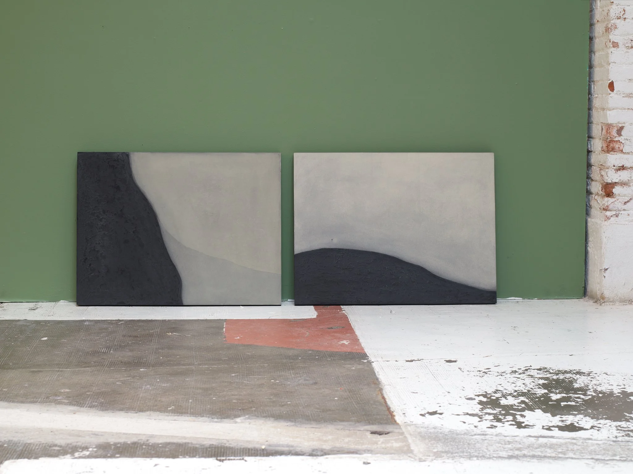 Two paintings with abstract designs leaning against a green wall in an unfinished room.