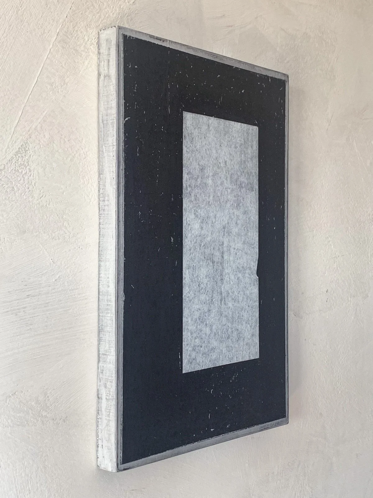 A vintage black and white screen printing frame with a rectangular mesh, mounted on a beige wall.