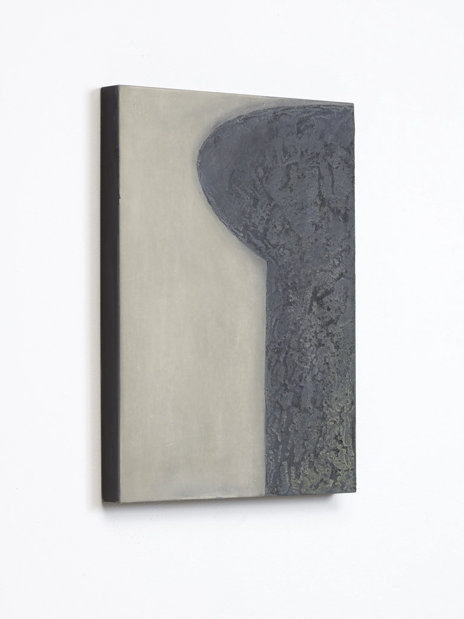 Close-up of abstract art piece with a curved dark gray shape on a light background, mounted on a white wall.