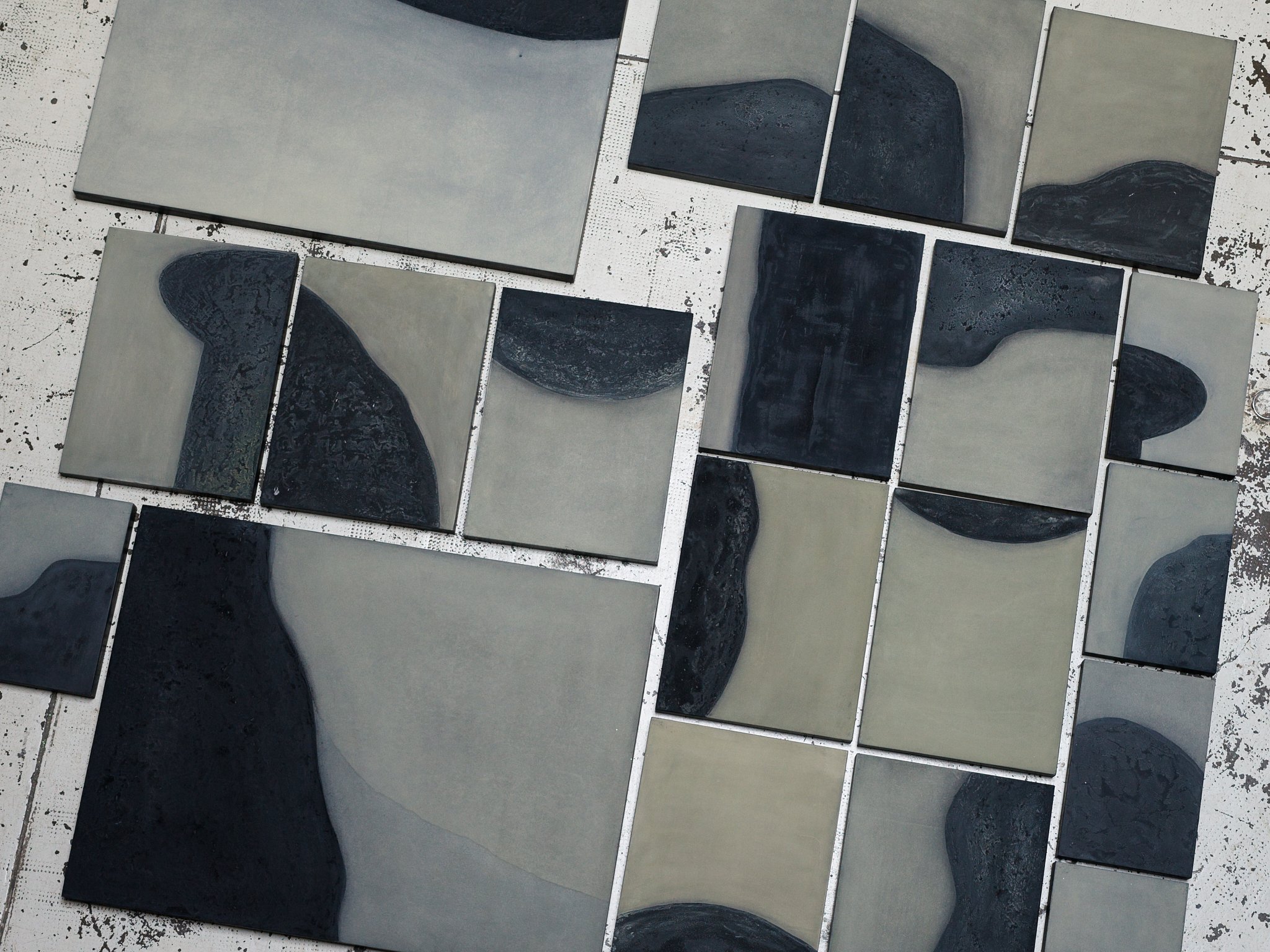 Several square tiles with black and gray abstract patterns are arranged on a white surface with black specks.