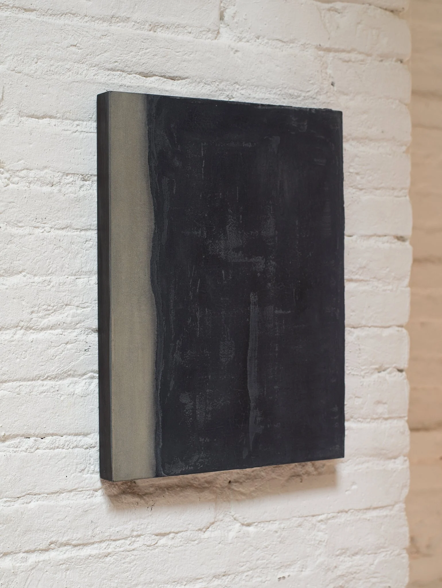 Close-up of a rectangular black and gray stone sculpture mounted on a white brick wall.