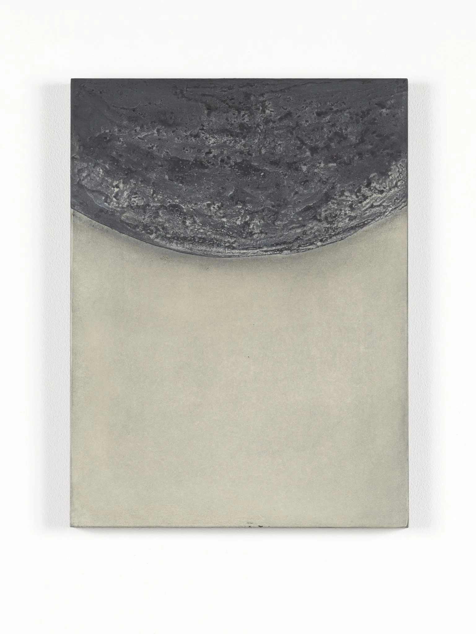 Close-up of a gray granite object with a semi-circular shape, positioned on a two-toned background with a white upper section and a gray lower section.