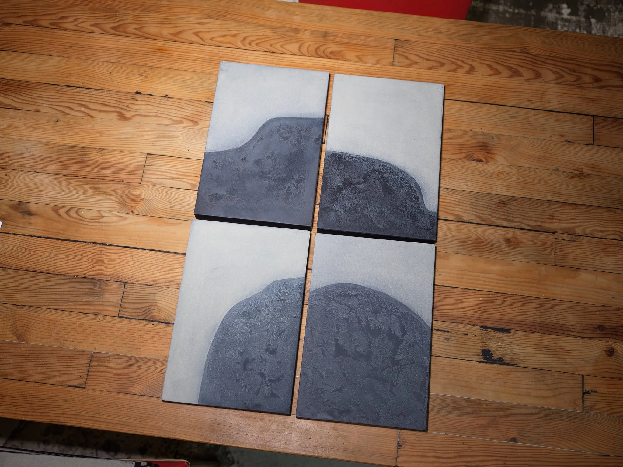 A partially completed tile wall on a wooden surface showing four tiles in shades of gray with a wave-like pattern.