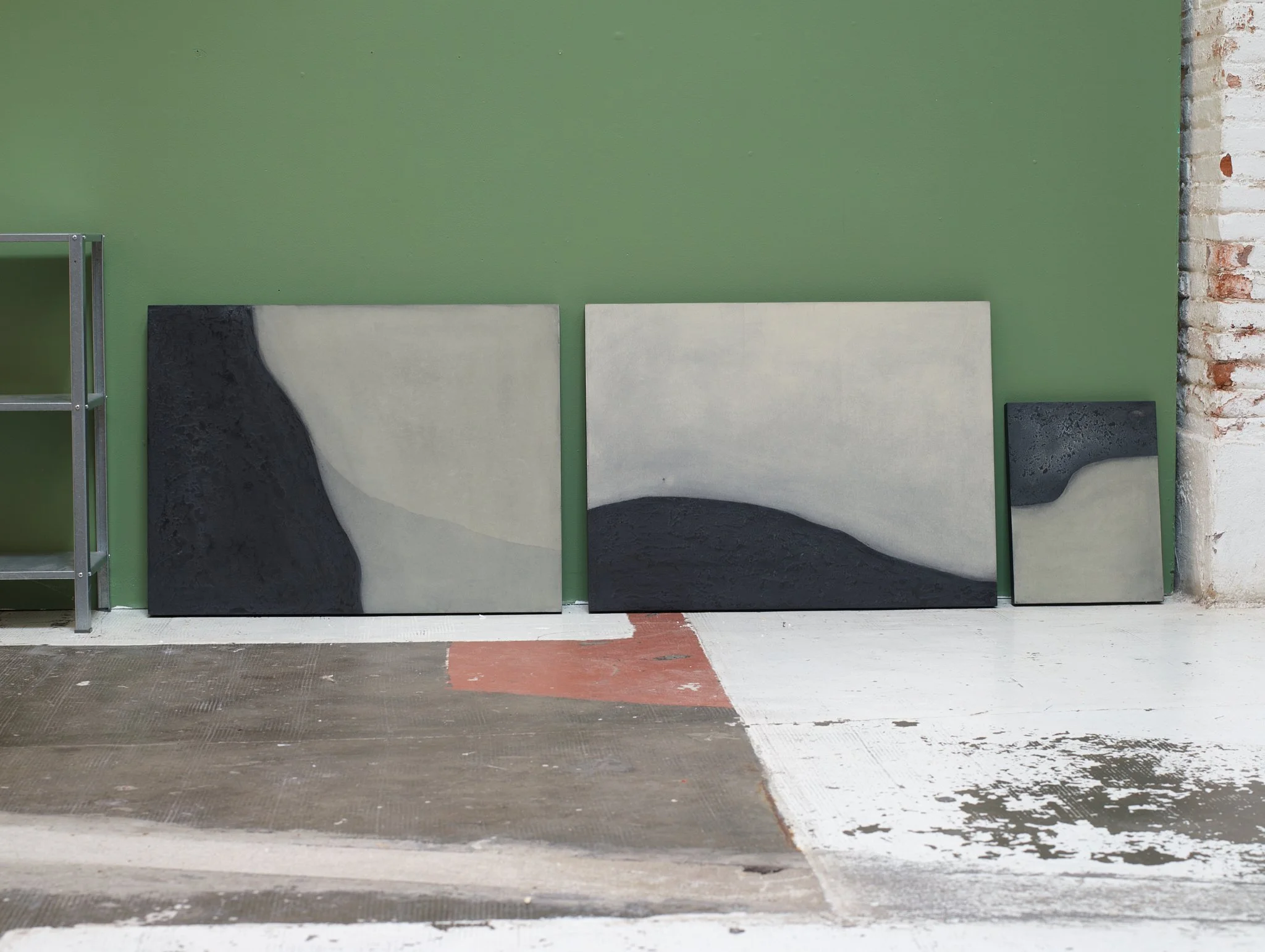 A row of three tiles, with one being black and white, against a green wall, beside a white brick wall with partially painted bricks.