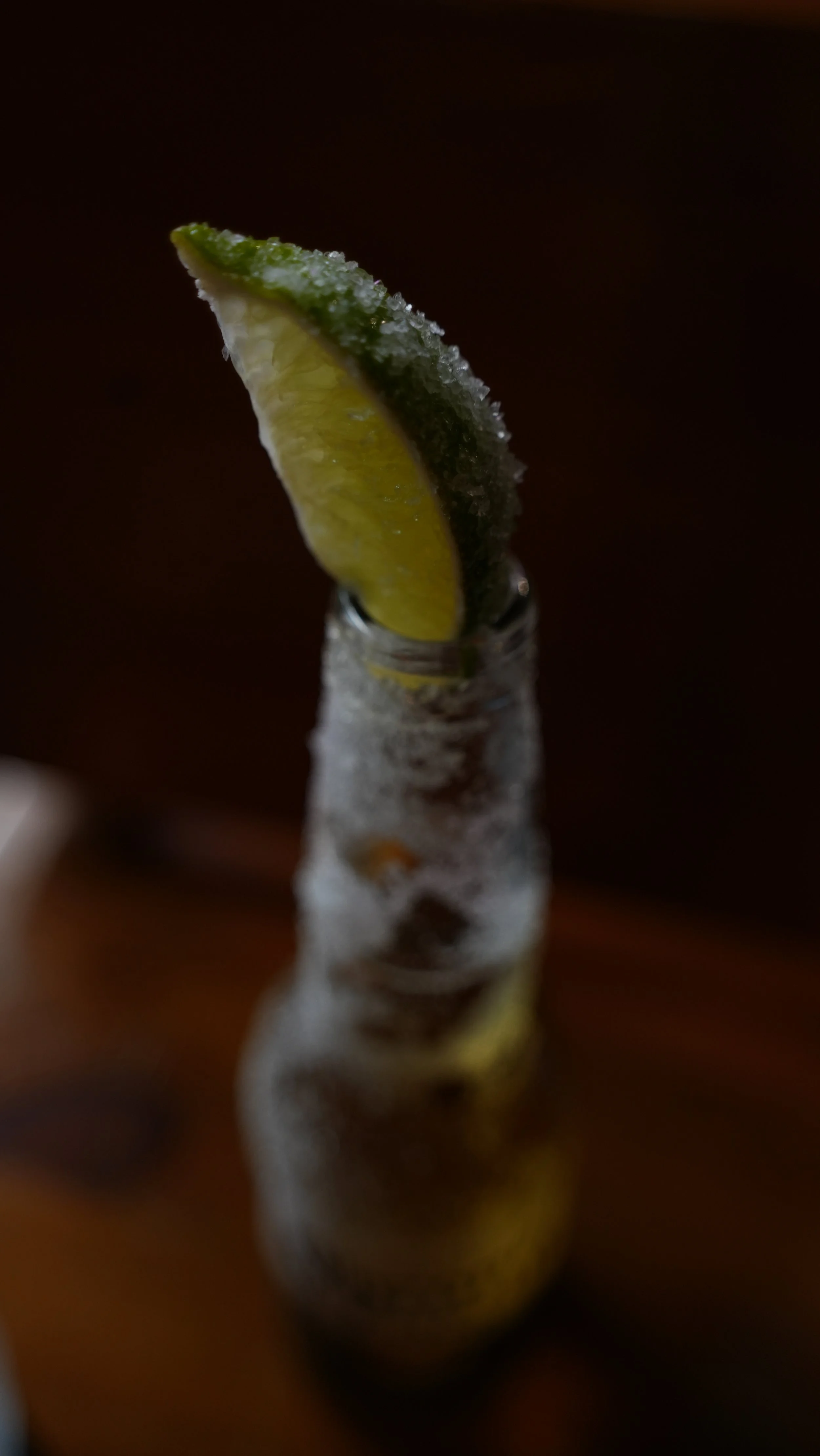 A lemon wedge frozen on top of a glass bottle of ice. The bottle is on a wooden surface.