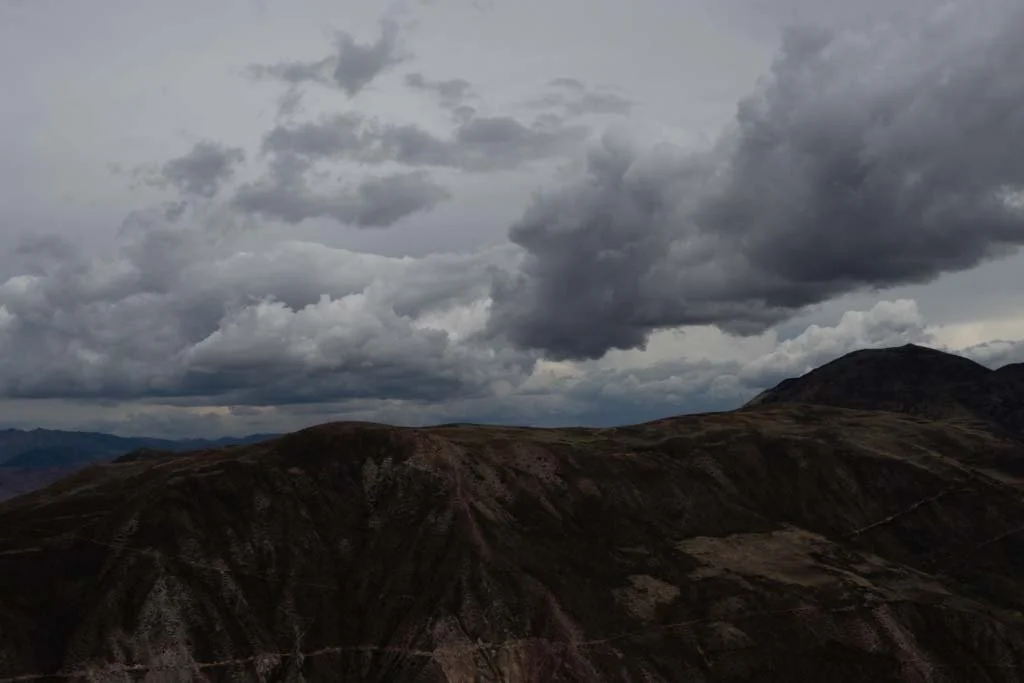 Dark, overcast sky with heavy clouds over a rugged mountainous landscape.