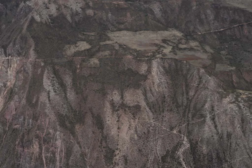 Aerial view of a mountainous terrain with sparse vegetation, dirt roads, and a few small bodies of water.