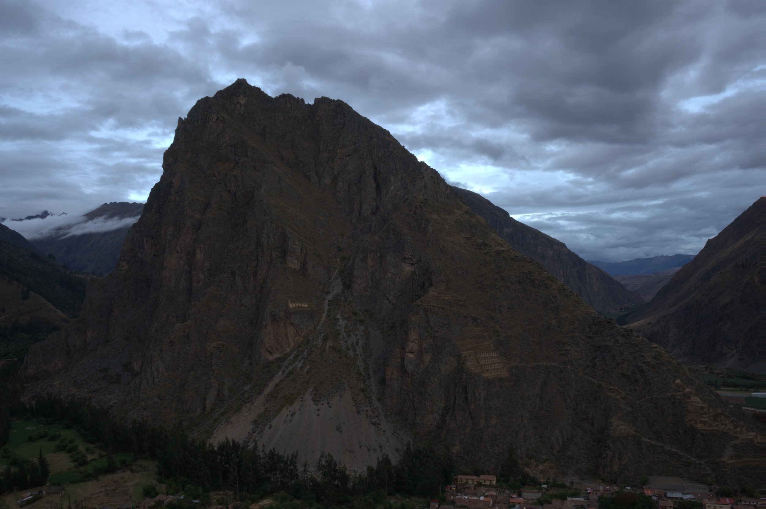 Cloudy mountain landscape with steep rocky peaks and a small village at the base.