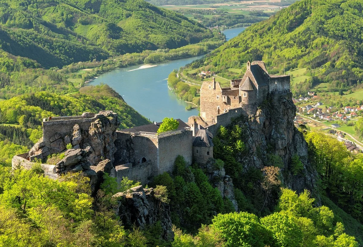 Burg auf einem Felsen mit Blick auf einen Fluss und grüne Hügel in einer ländlichen Gegend.