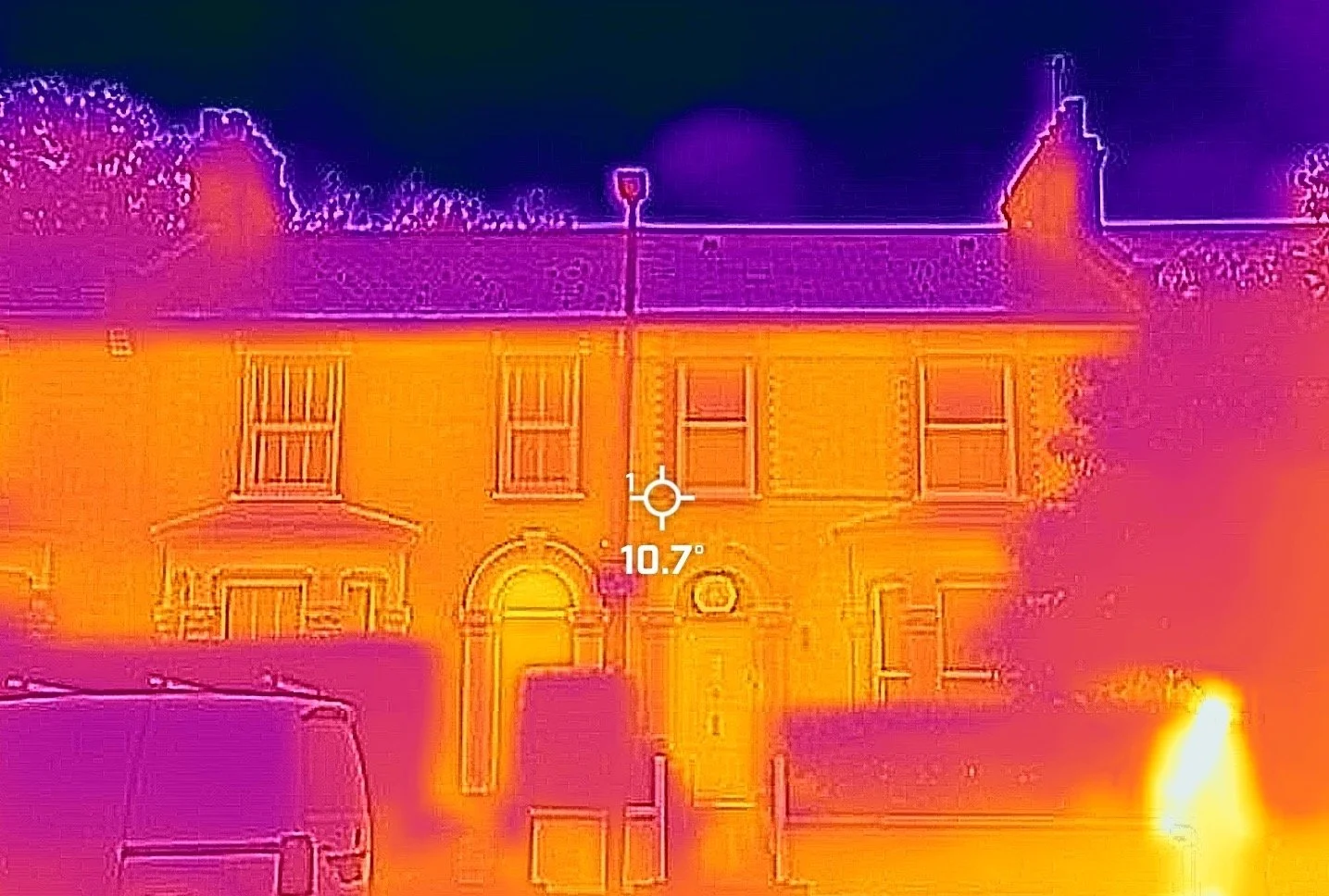Infrared thermal image of a house showing warm and cold areas, including vehicles parked out front and trees surrounding the building.