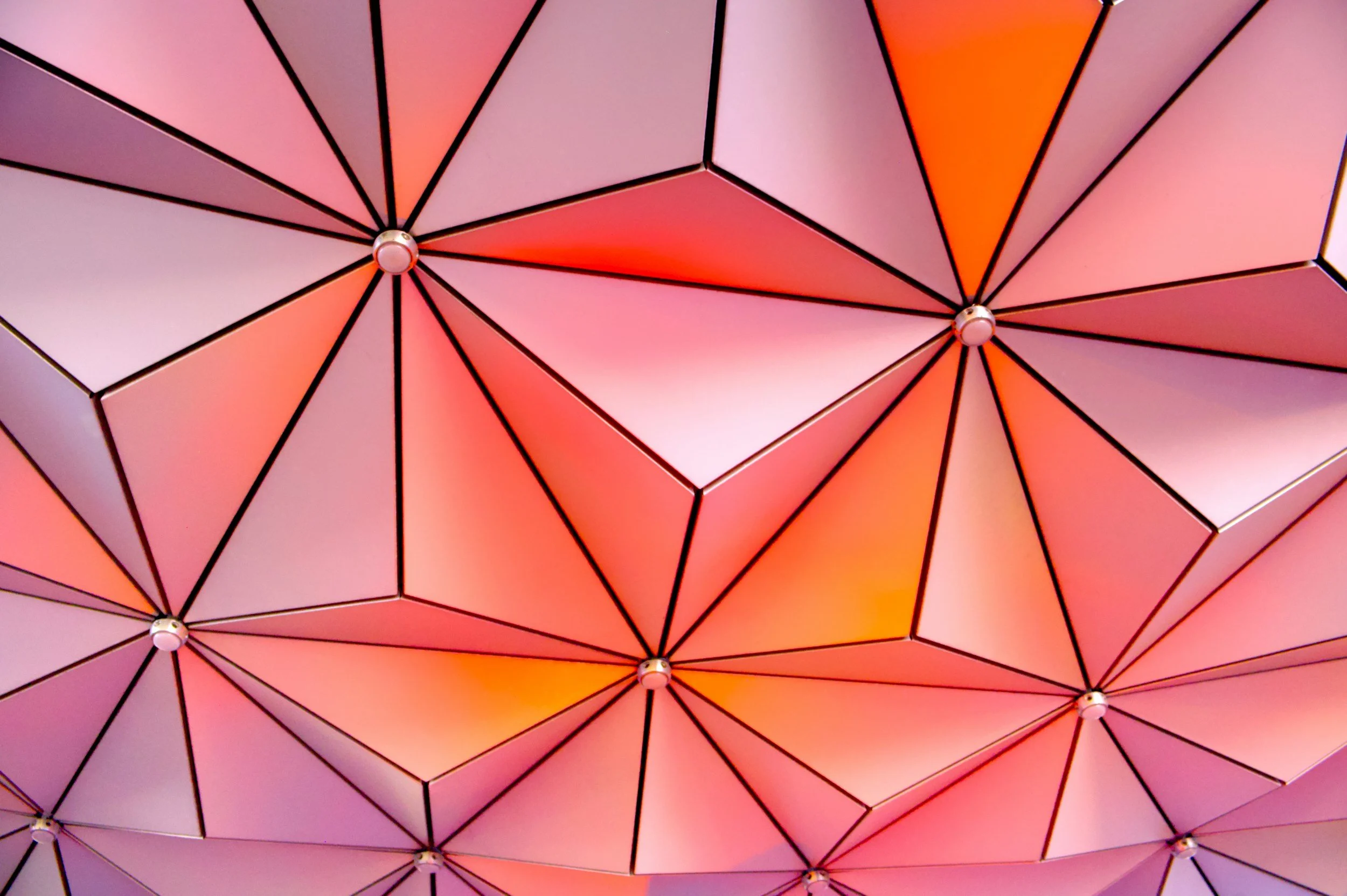Close-up of a geometric dome made of panels in pink, orange, and purple shades, with black outlines and small circular connectors at the intersections.