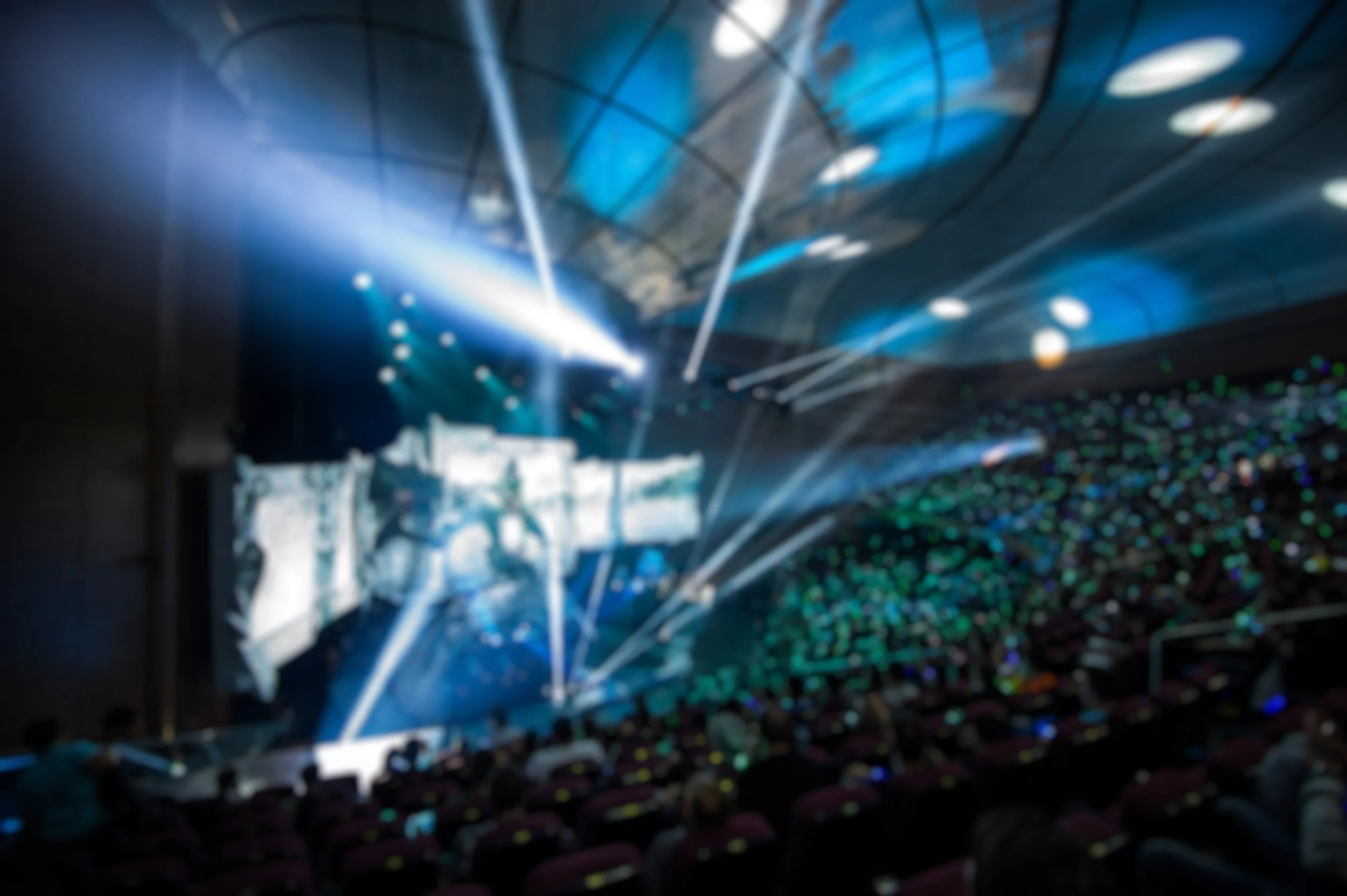 A blurry image of a crowded event with stage lights and laser beams in a large indoor venue.