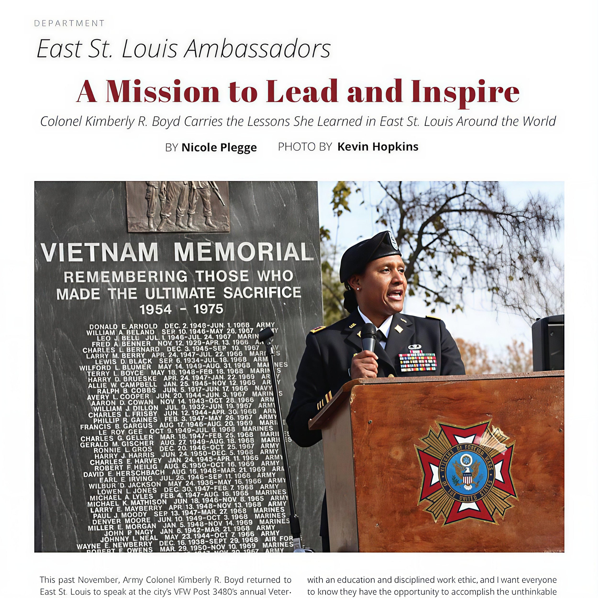 Army officer speaking in front of a Vietnam Memorial with a list of names and a Vietnam War emblem.