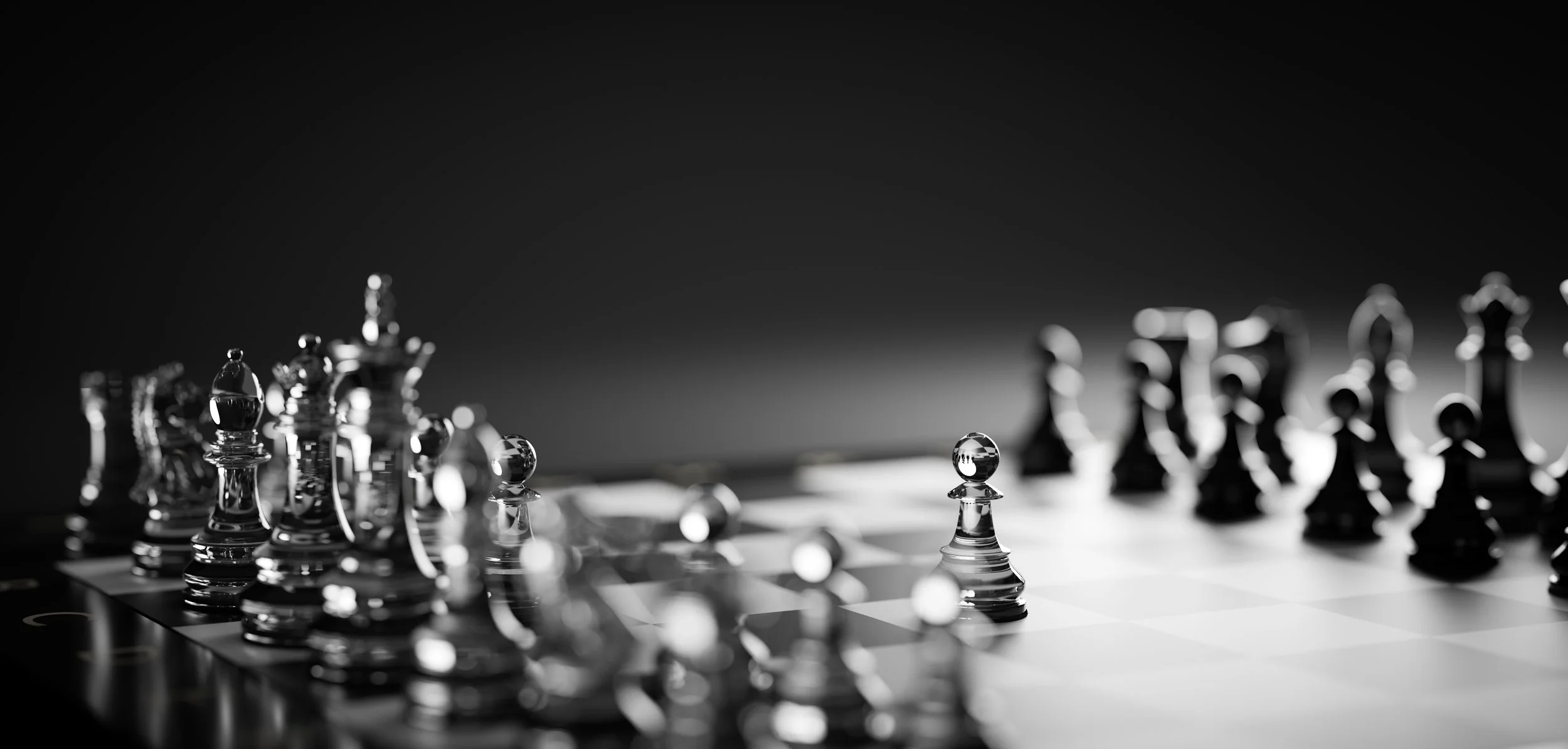 Black and white photograph of a chessboard with glass chess pieces, showing the pieces in mid-game with some captured. The scene is dark and moody, with a shallow depth of field focusing on a crystal pawn.
