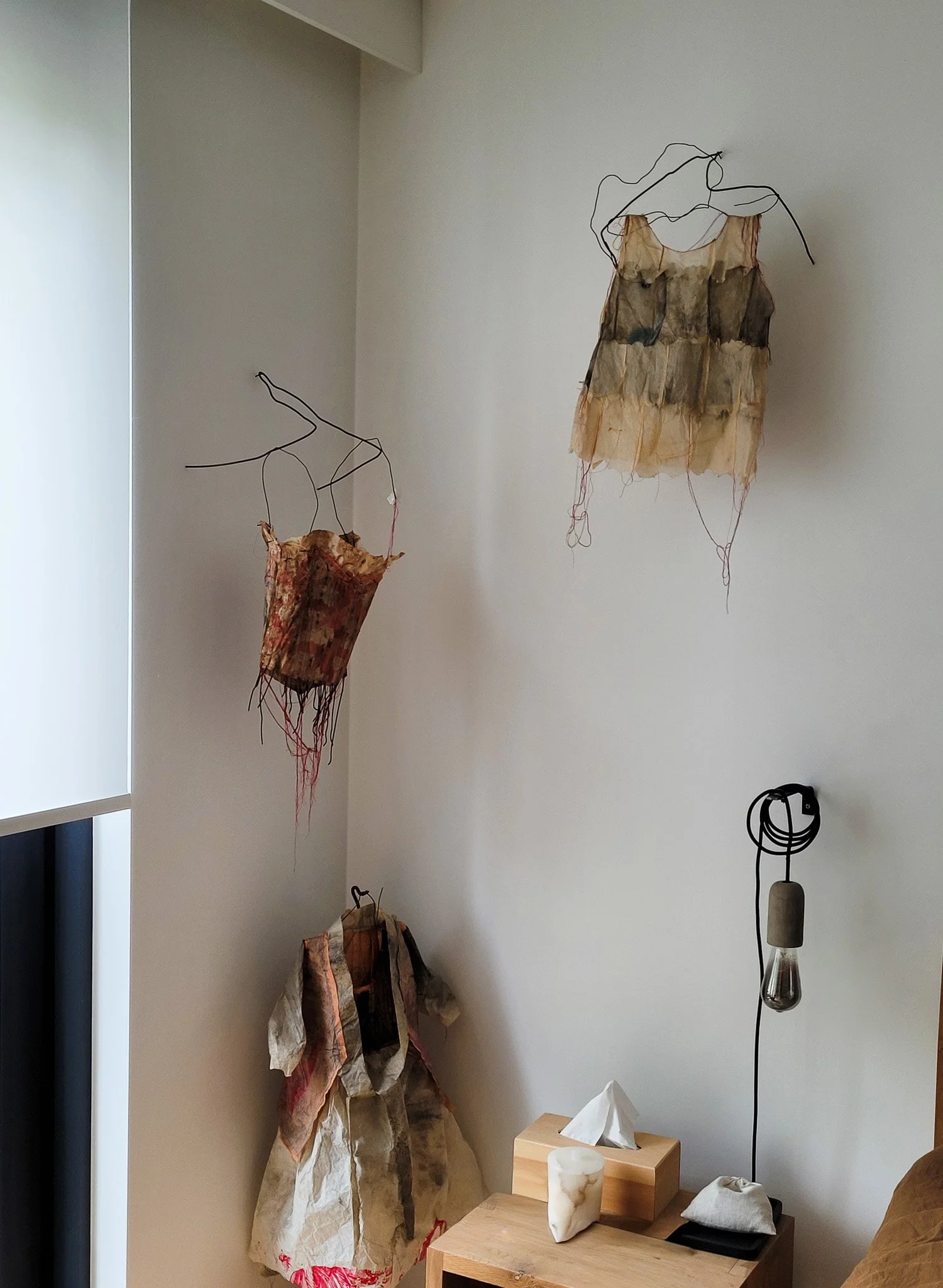 Décoration murale artistique avec des sculptures en fil métallique et tissu suspendues dans une pièce intérieure.