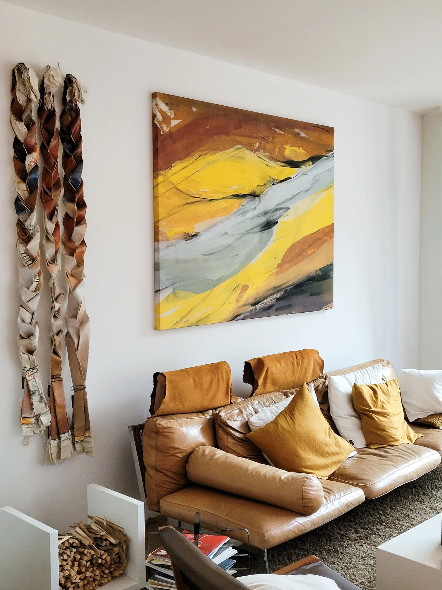 Salon avec un canapé en cuir beige, des coussins jaunes et blancs, un tableau abstrait aux tons jaune de l'artiste Maqua , gris, blanc et noir, et des blocs de bois empilés