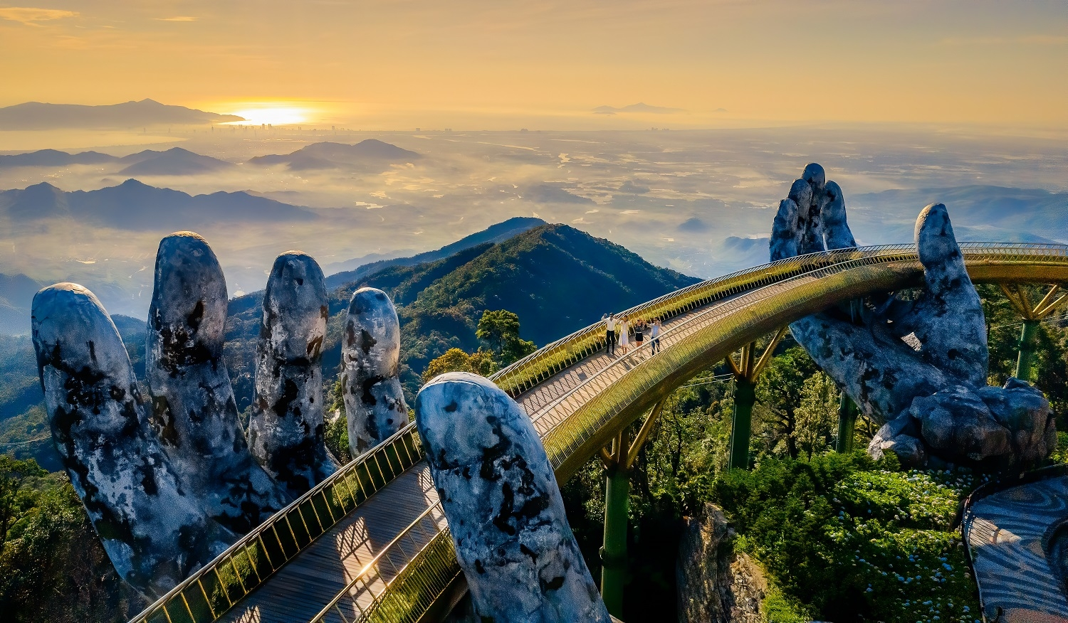A futuristic pedestrian bridge supported by giant hand-shaped structures, with a scenic mountain landscape and sunset in the background.