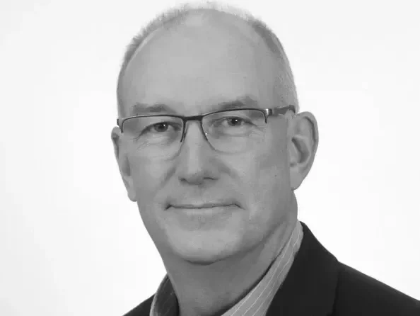Man in a suit with a floral boutonnière smiling at a formal event.