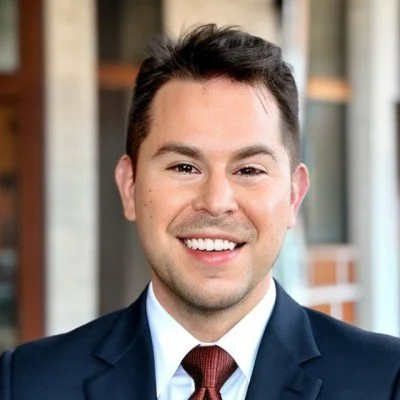 Person with glasses smiling in front of a bookshelf filled with books.