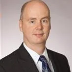 Smiling man in a suit and glasses against a plain background