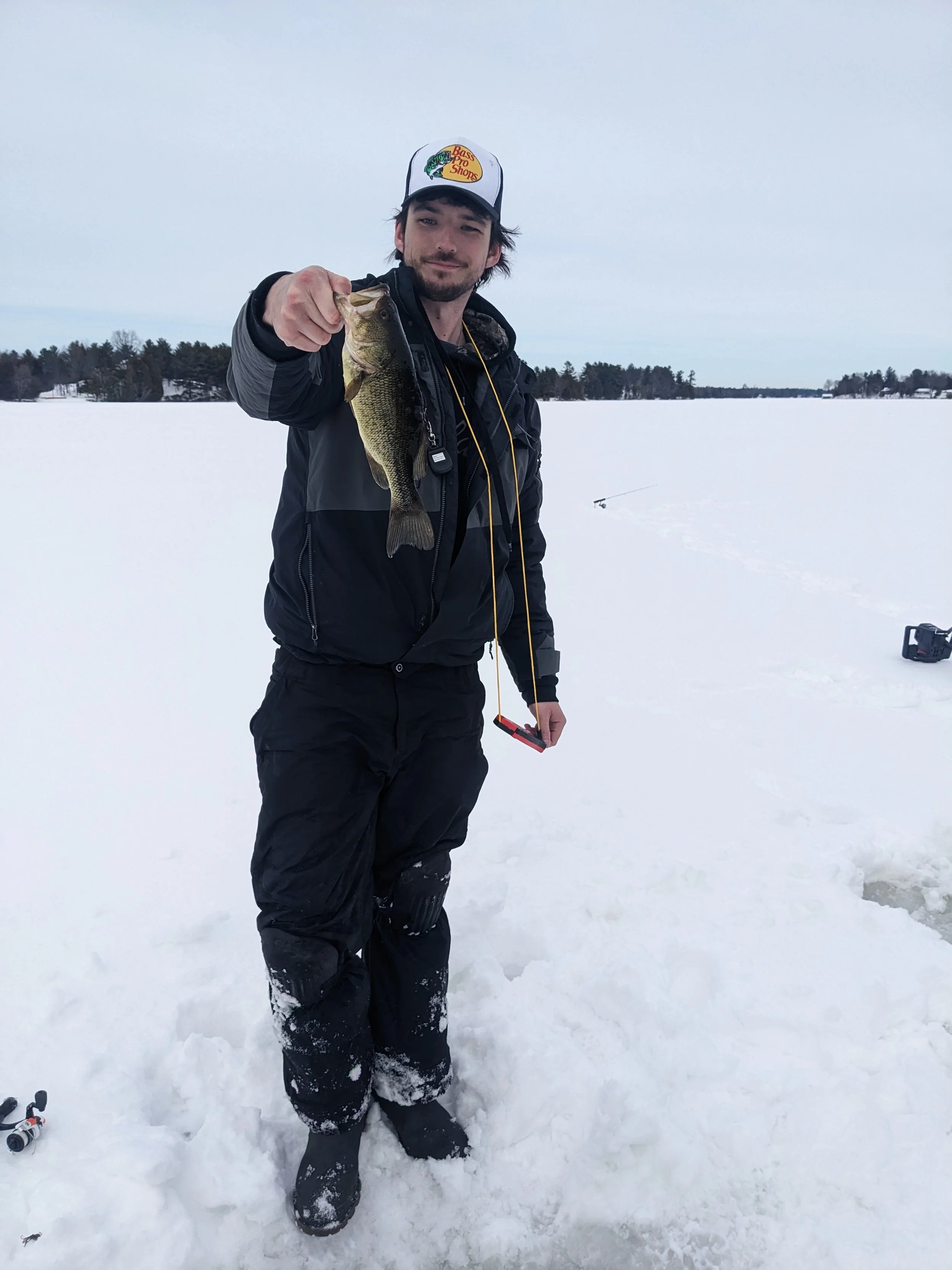 Man holding a fish he caught while ice fishing on a snowy lake.