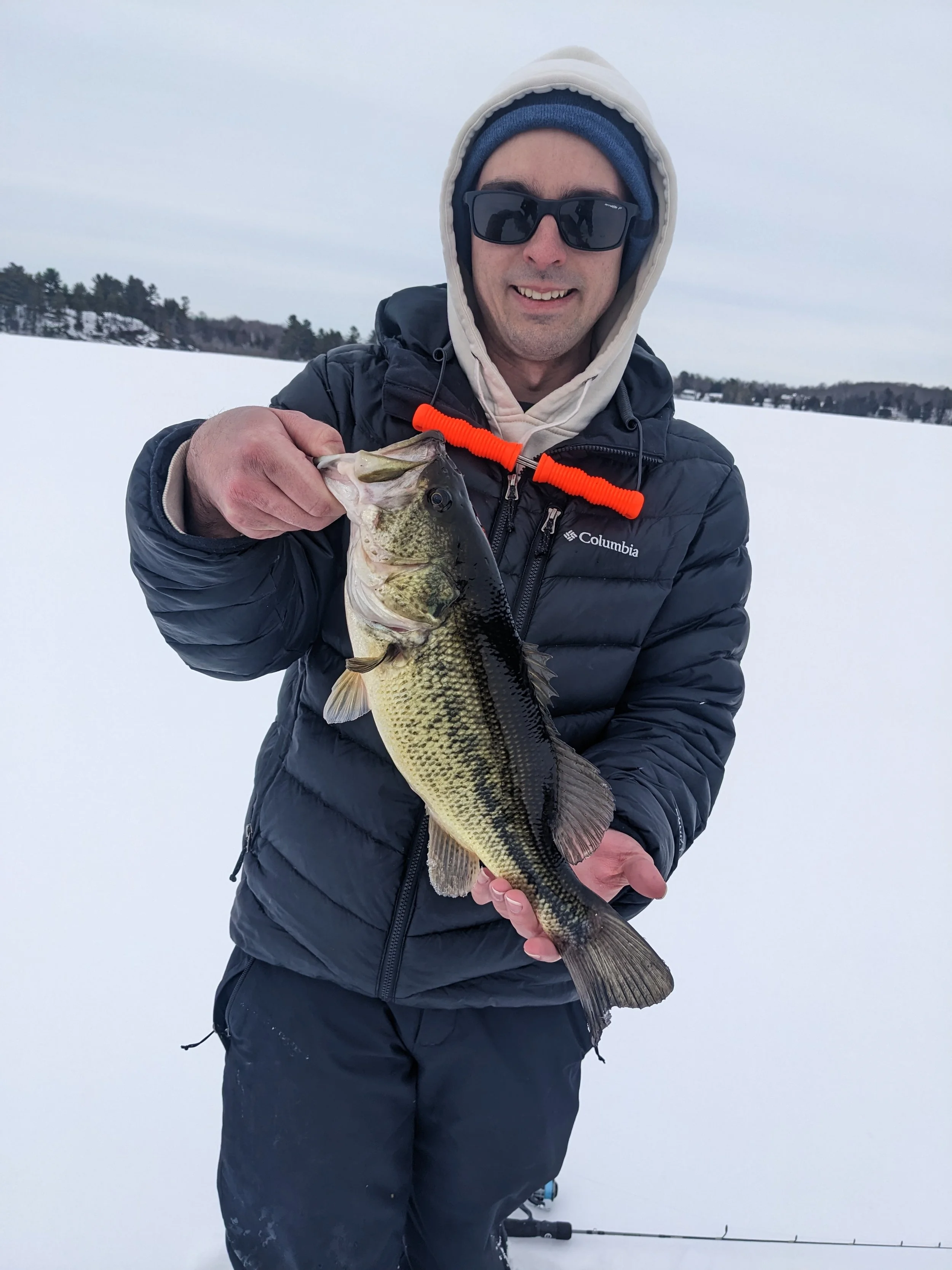 Man dressed in winter gear holding a large fish on snow-covered lake during winter.