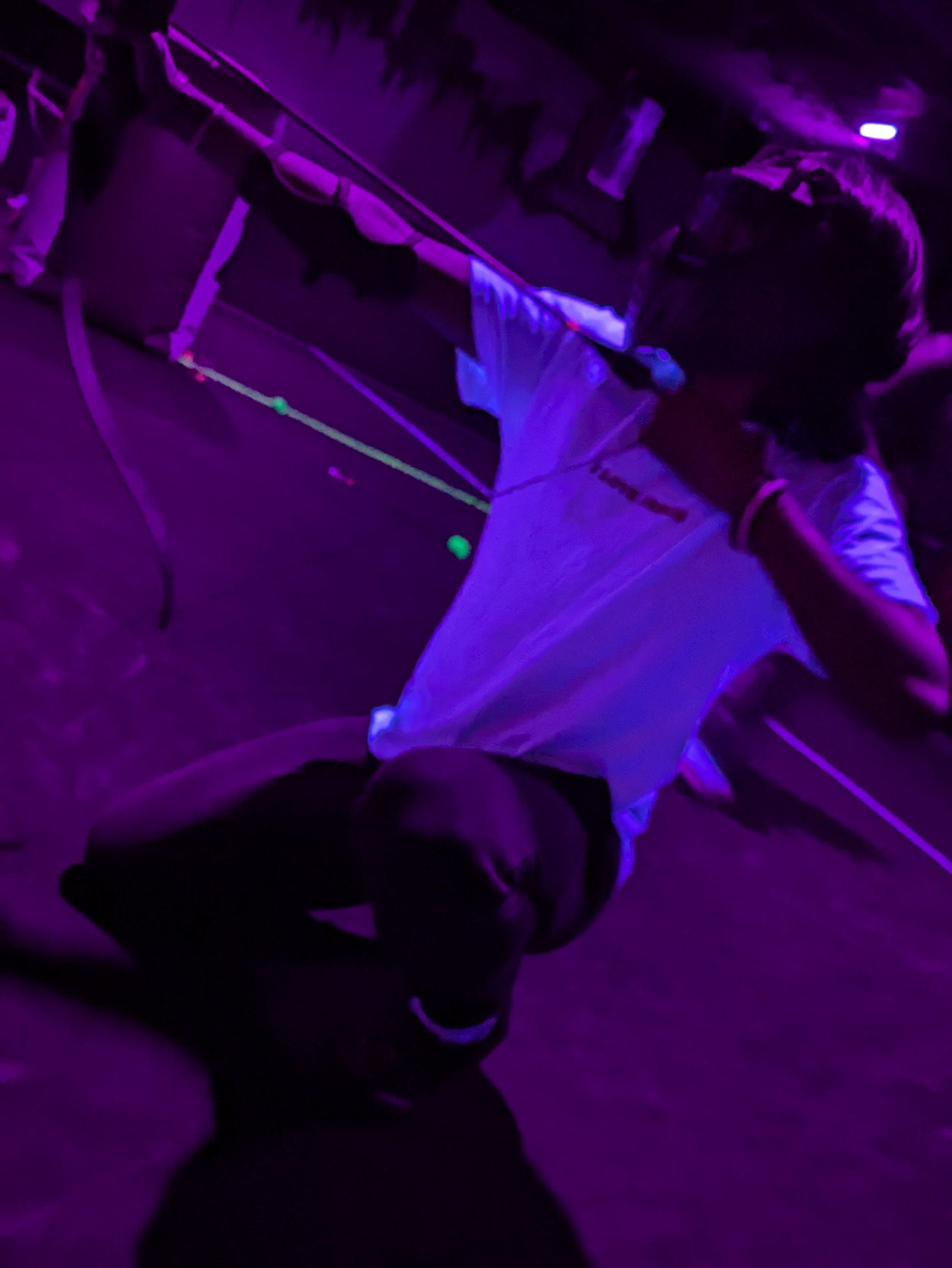Person playing archery in a dark room illuminated with blacklight