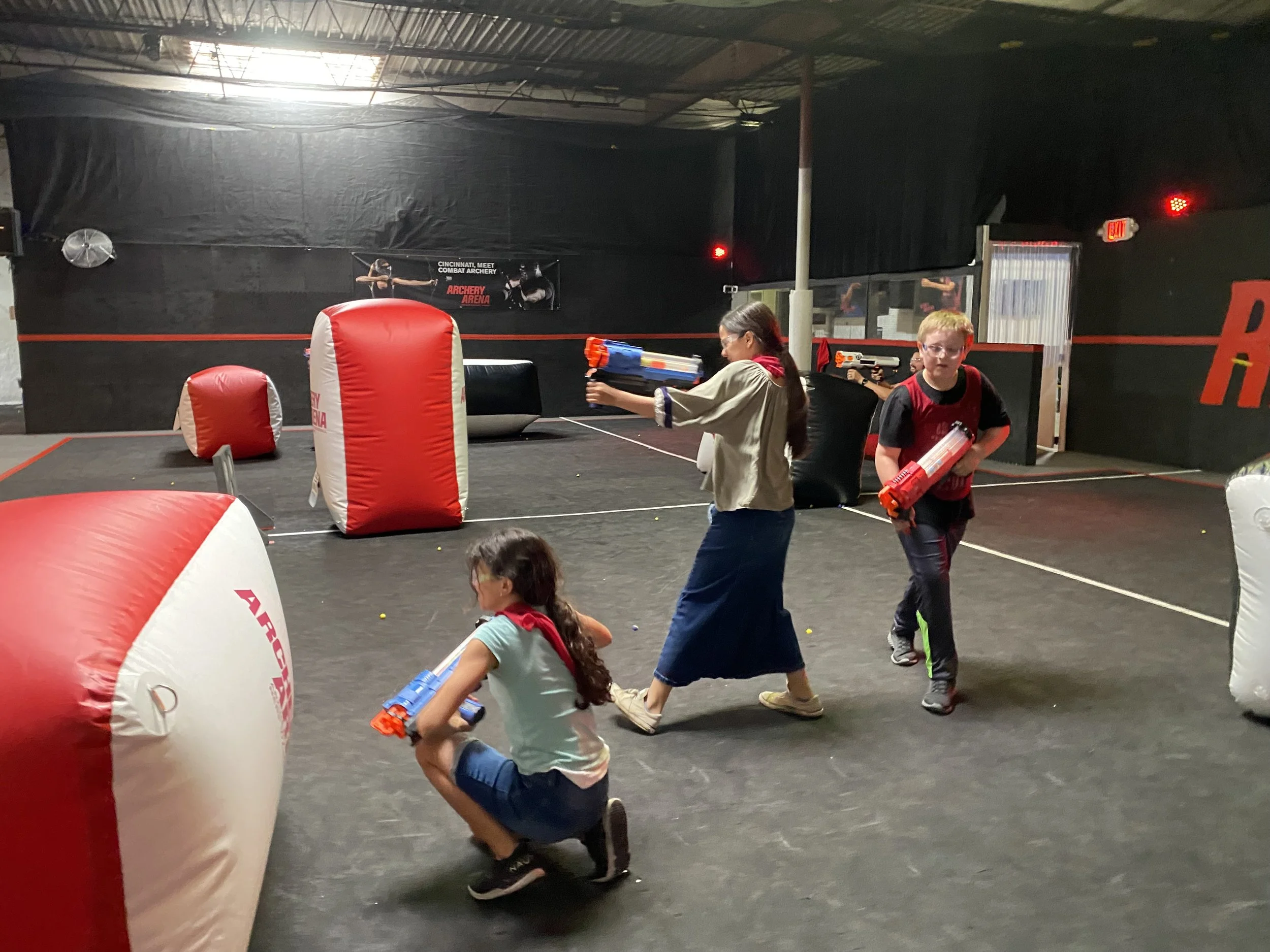 Children playing laser tag in an indoor arena with inflatable barriers and laser guns.