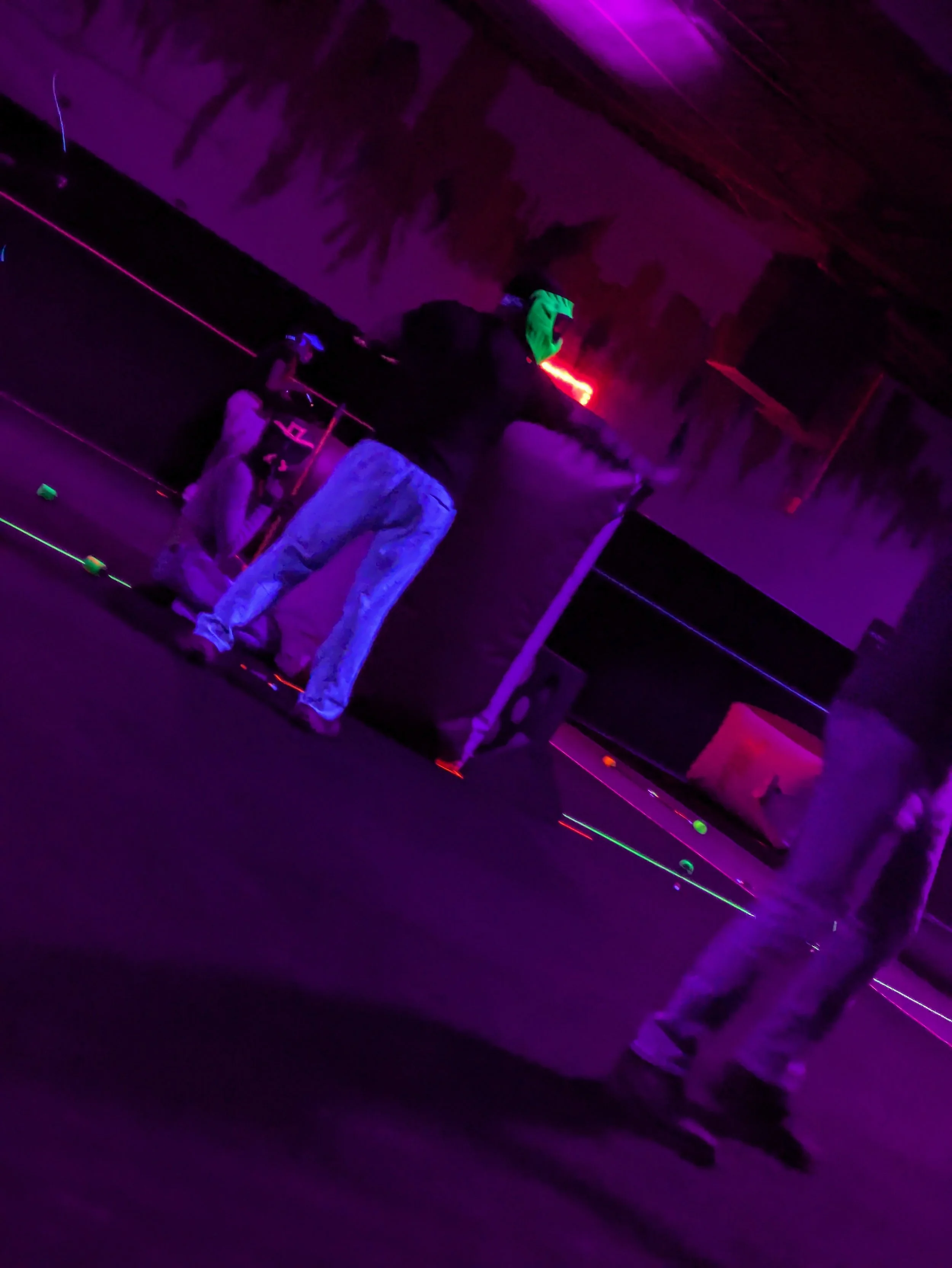 People wearing neon-colored clothing and accessories in a dark room with vibrant purple and pink lighting.