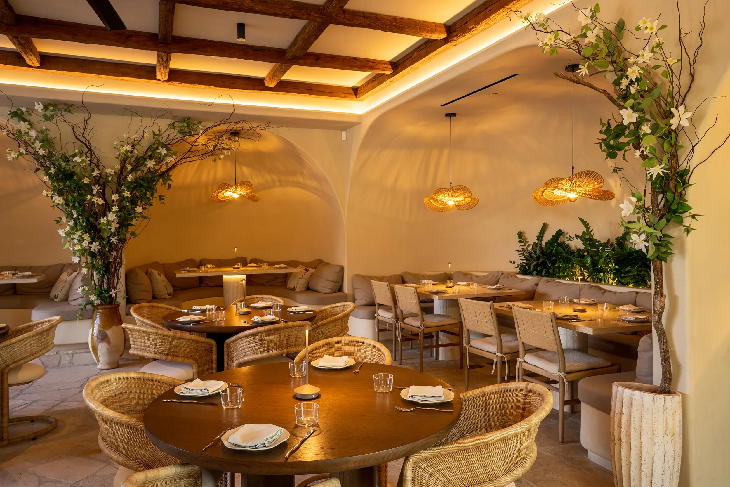 Curved banquette and rattan seating in the cove-lit main dining room at By The Sea