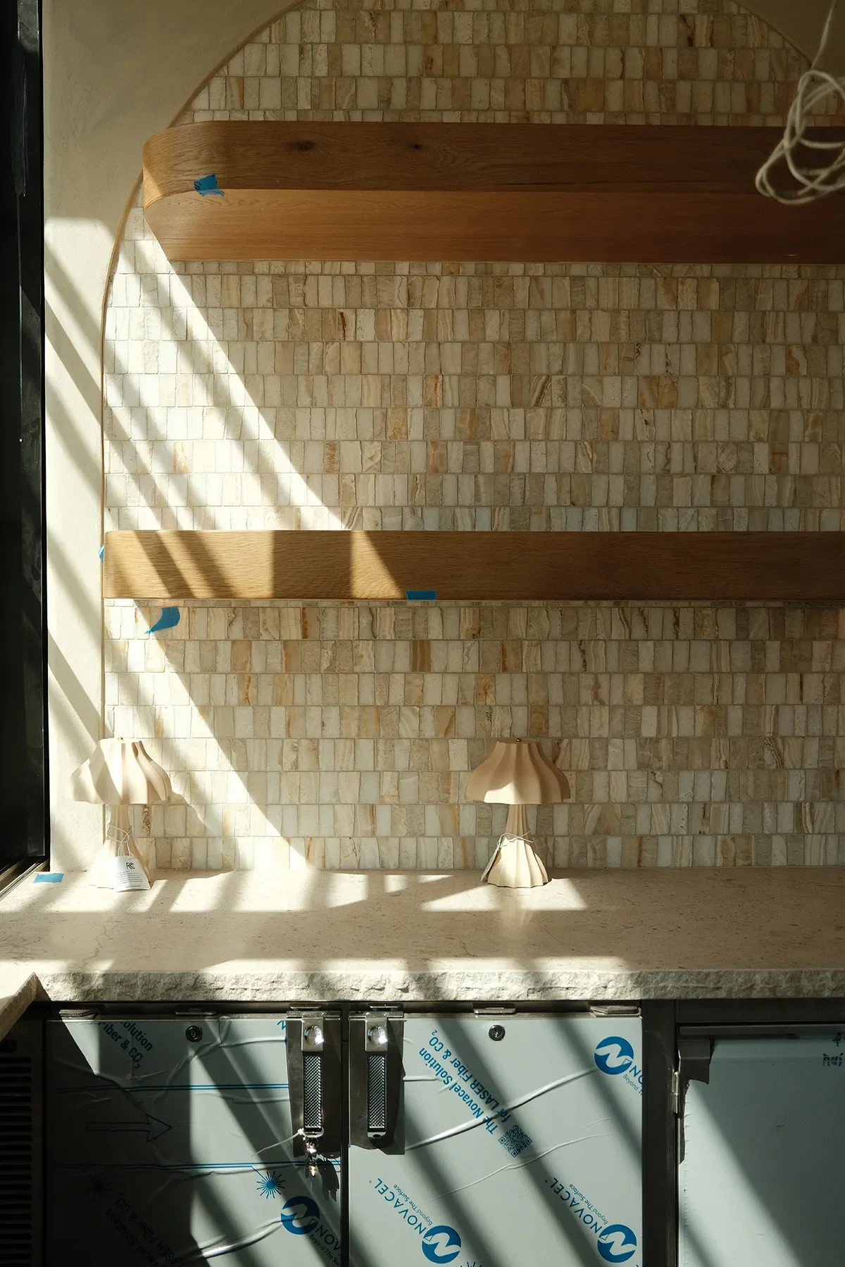 The arched mosaic tile panel with oak wood shelving going in above the bar cabinetry at By The Sea, Coronado