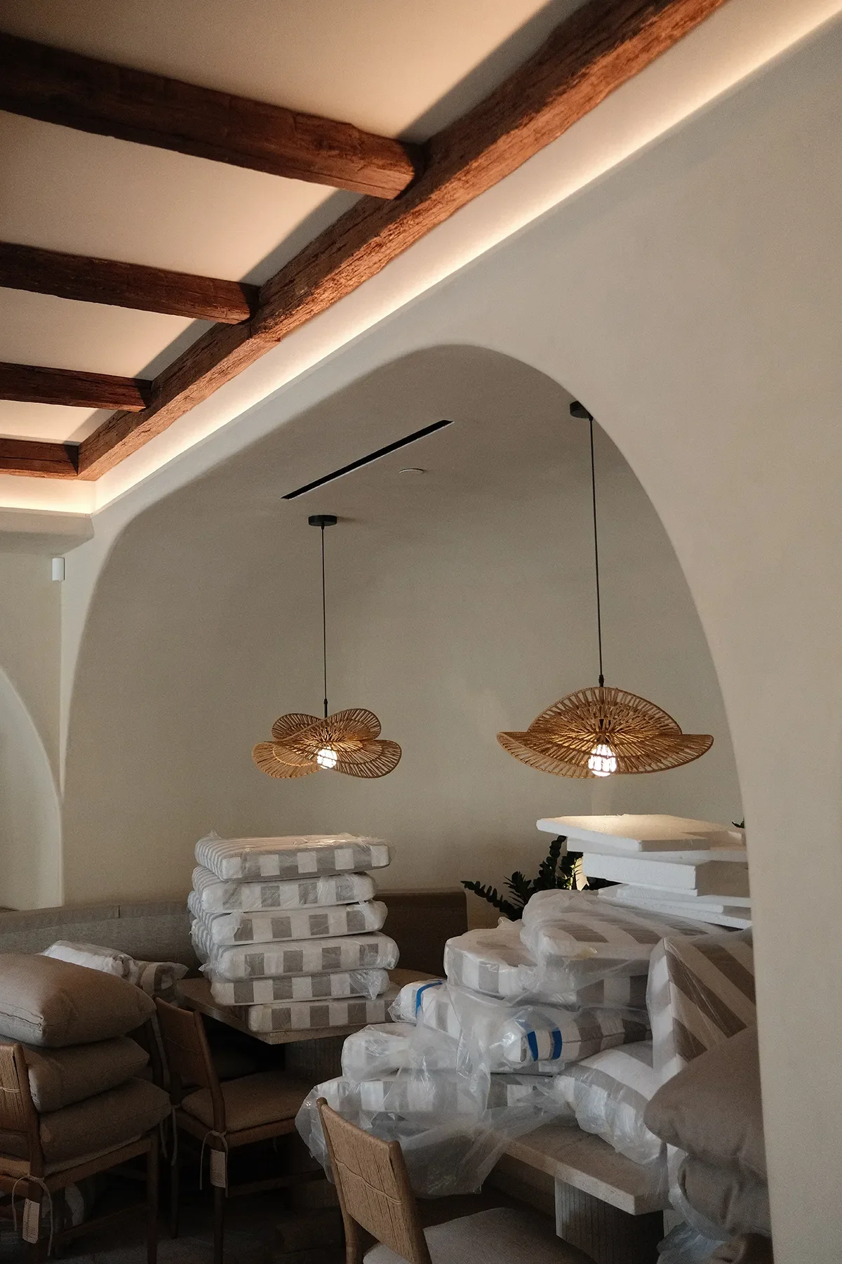 Wrapped seat cushions stacked under lit rattan pendants during the final install at By The Sea