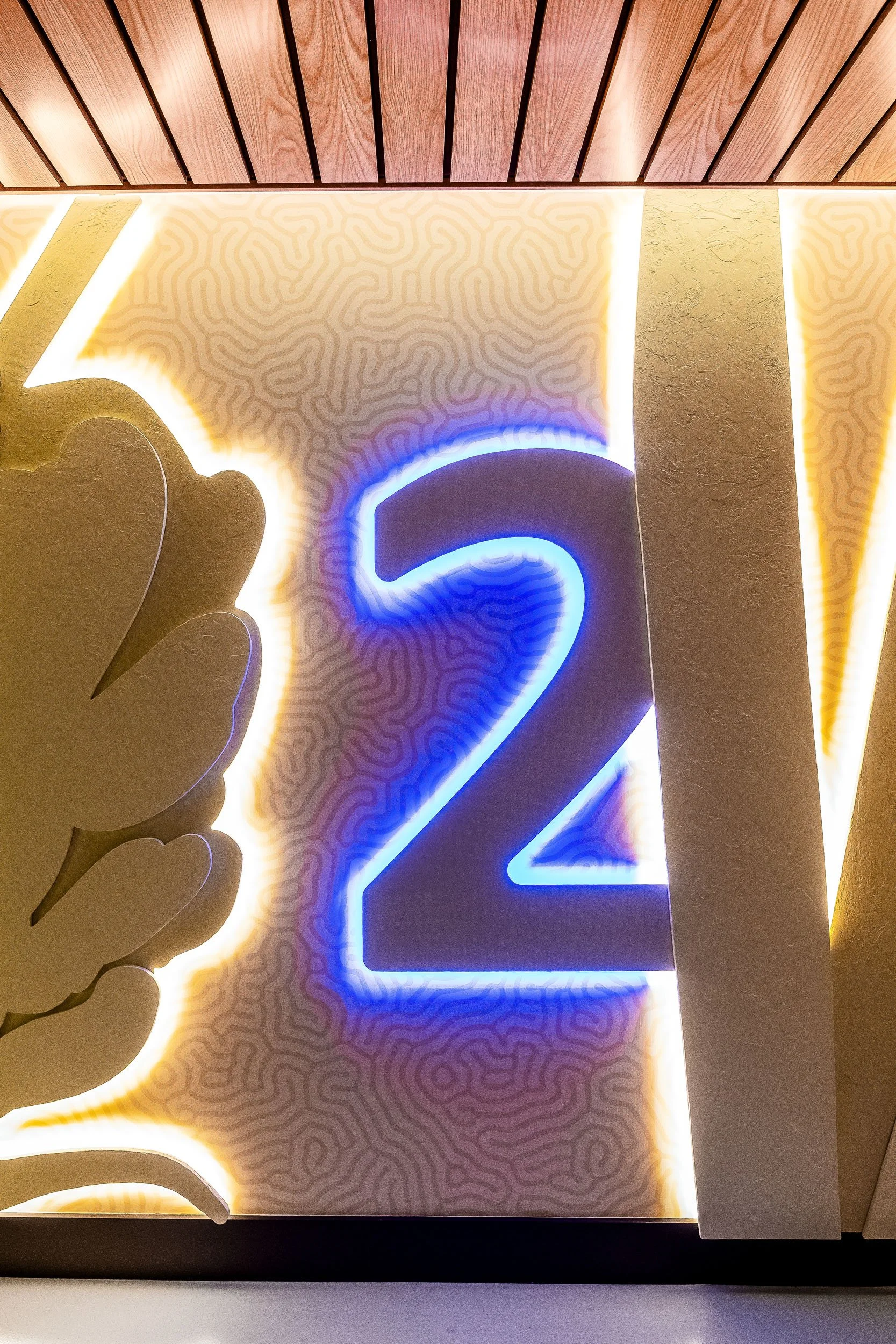 Illuminated blue floor number integrated into a layered paneled wall with sculptural lighting.